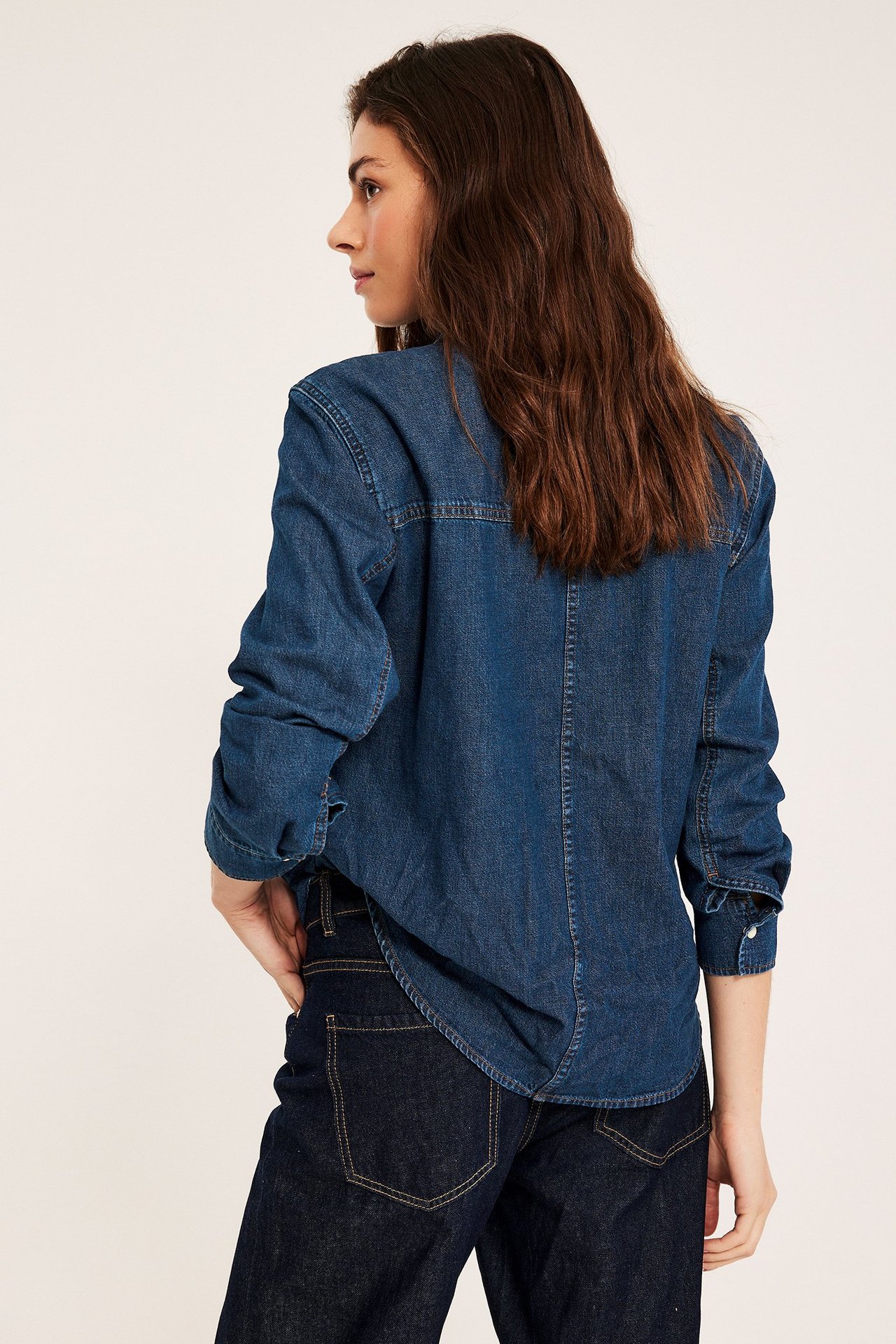 Side-/bakfra av kvinne i mørk denim bomullsskjorte med lange ermer, matchet med mørke jeans.