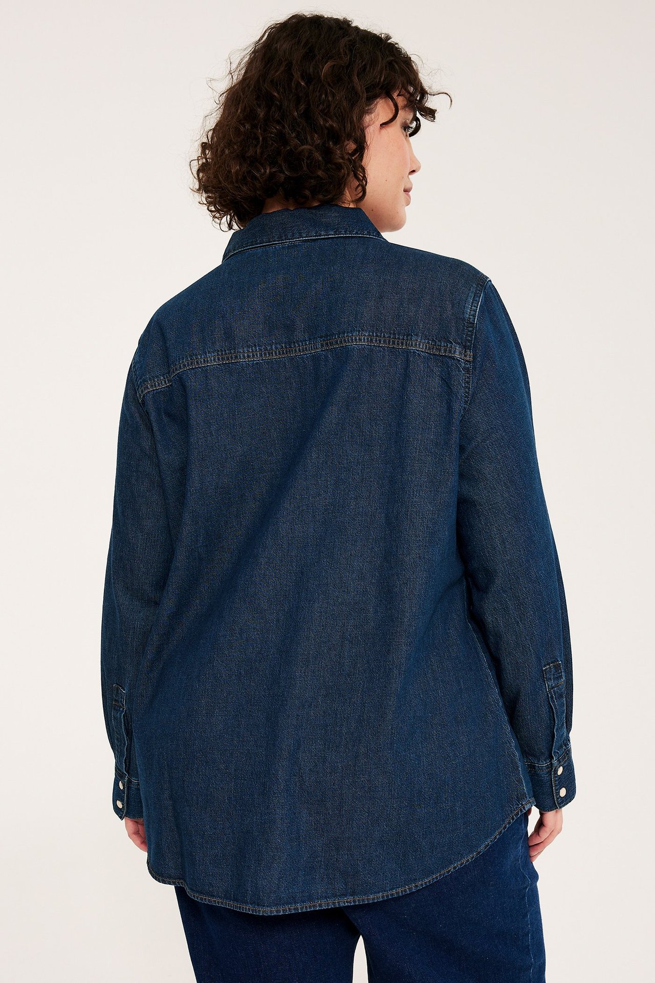 Takakuva naisesta tummansinisessä puuvillafarkkupaidassa, jossa painonapit hihoissa.