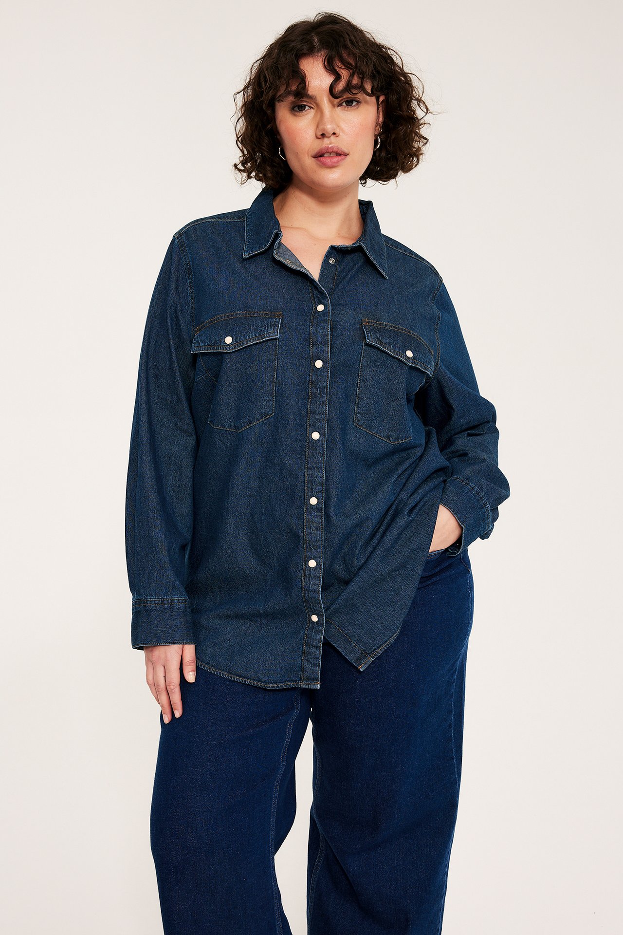 Edestä kuvattuna: nainen tummansinisessä farkkupaidassa neppareilla ja yhteensopivissa tummansinisissä farkuissa.