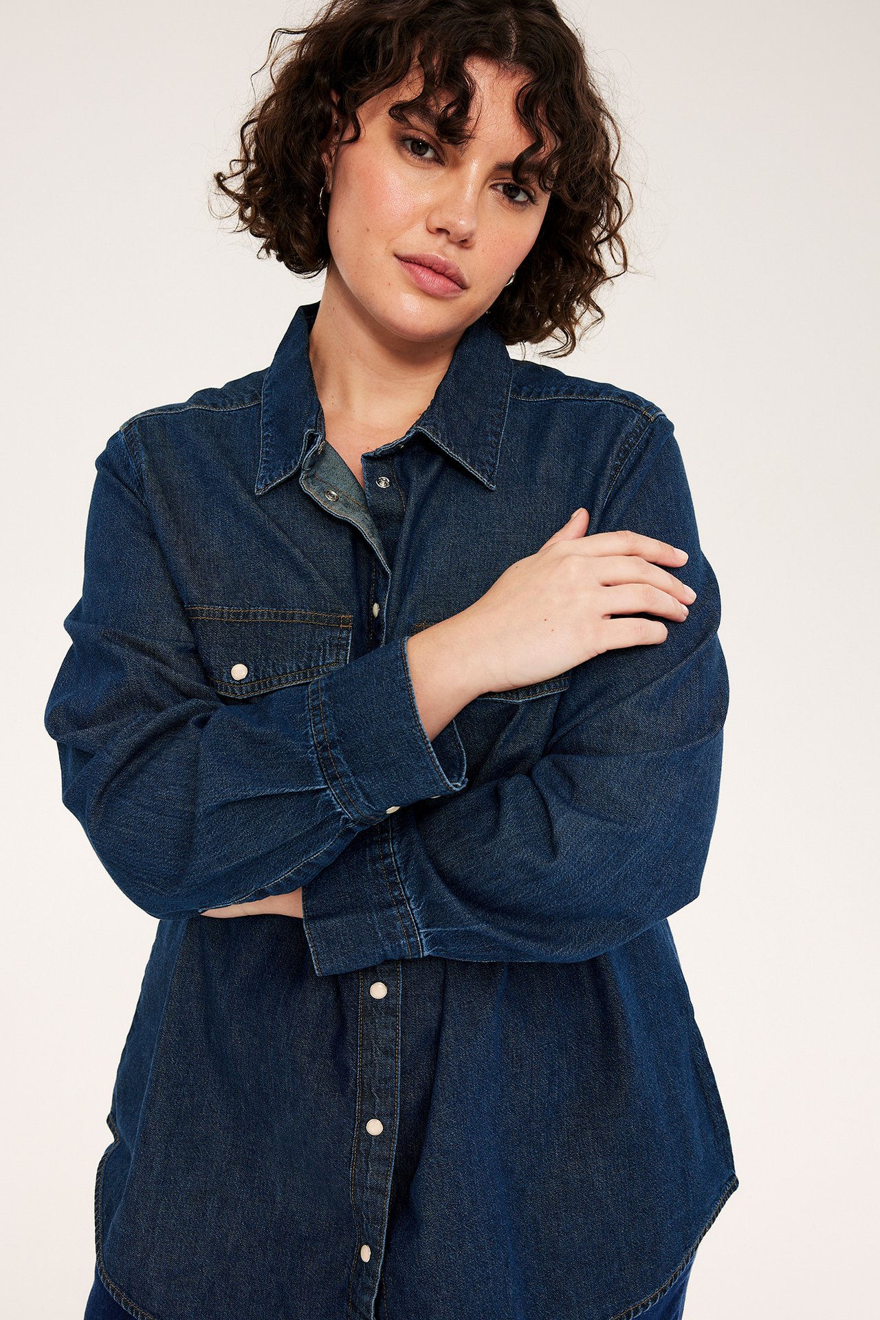 Edestäpäin, nainen tummansinisessä farkkupaidassa, jossa valkoiset nepparit ja rintataskut.