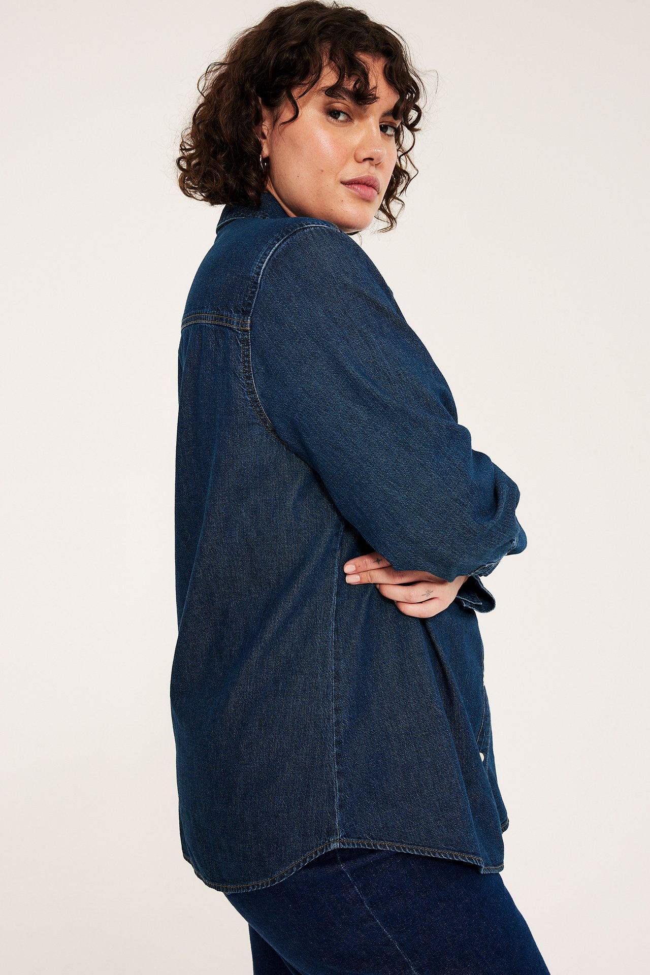 Sivukuva naisesta yllään rento tummansininen puuvillainen farkkupaita neppareilla ja yhteensopivat farkut.