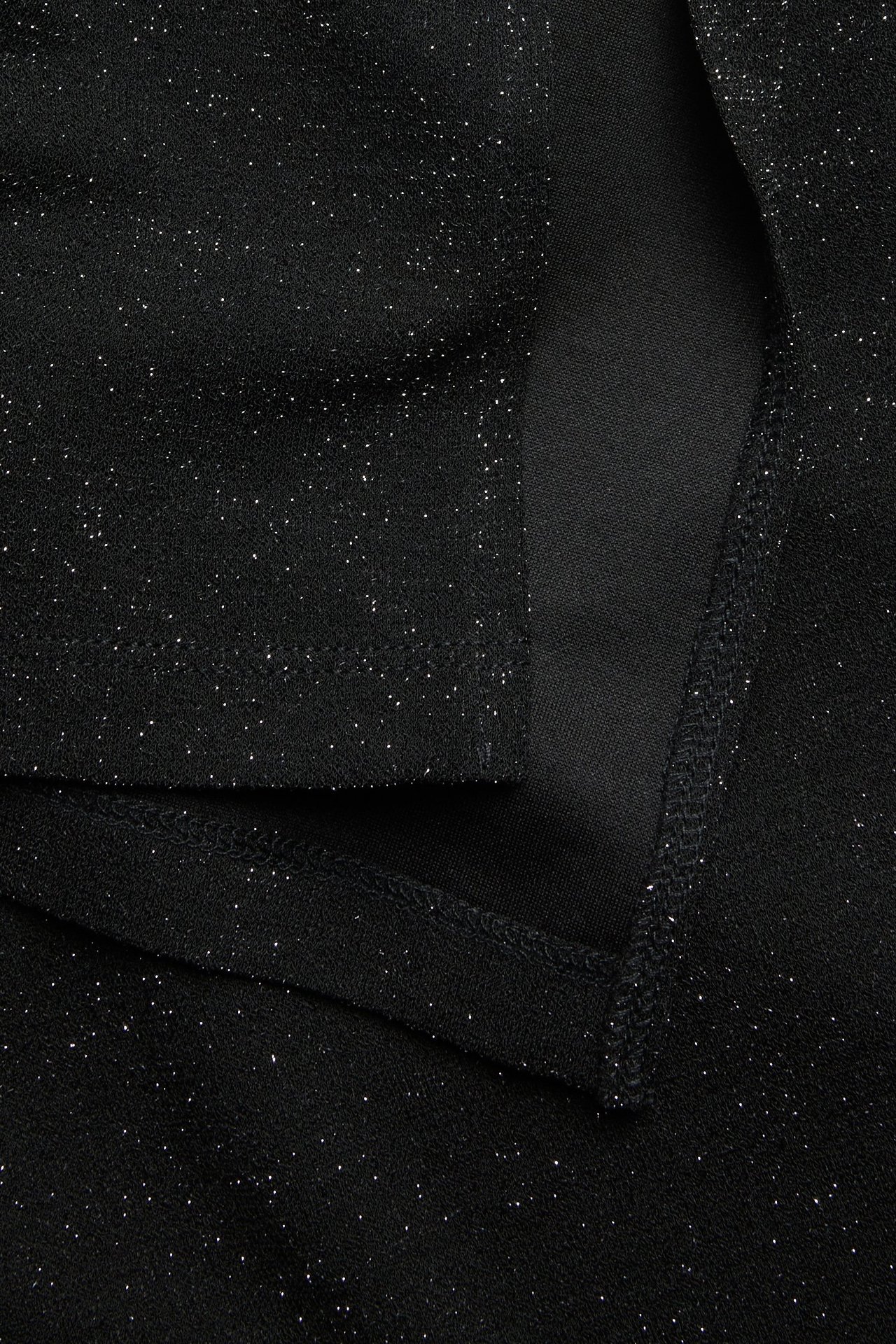 Zbliżenie czarnej, brokatowej długiej spódnicy, ukazujące błyszczący materiał lurex z drobnymi iskierkami.