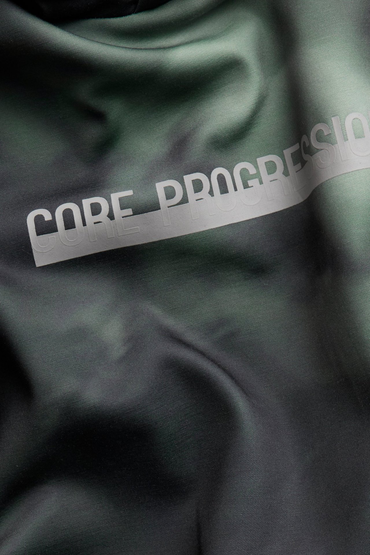 Zbliżenie na zieloną, wzorzystą bluzę z kapturem interlock z napisem "CORE PROGRESSION" z przodu.