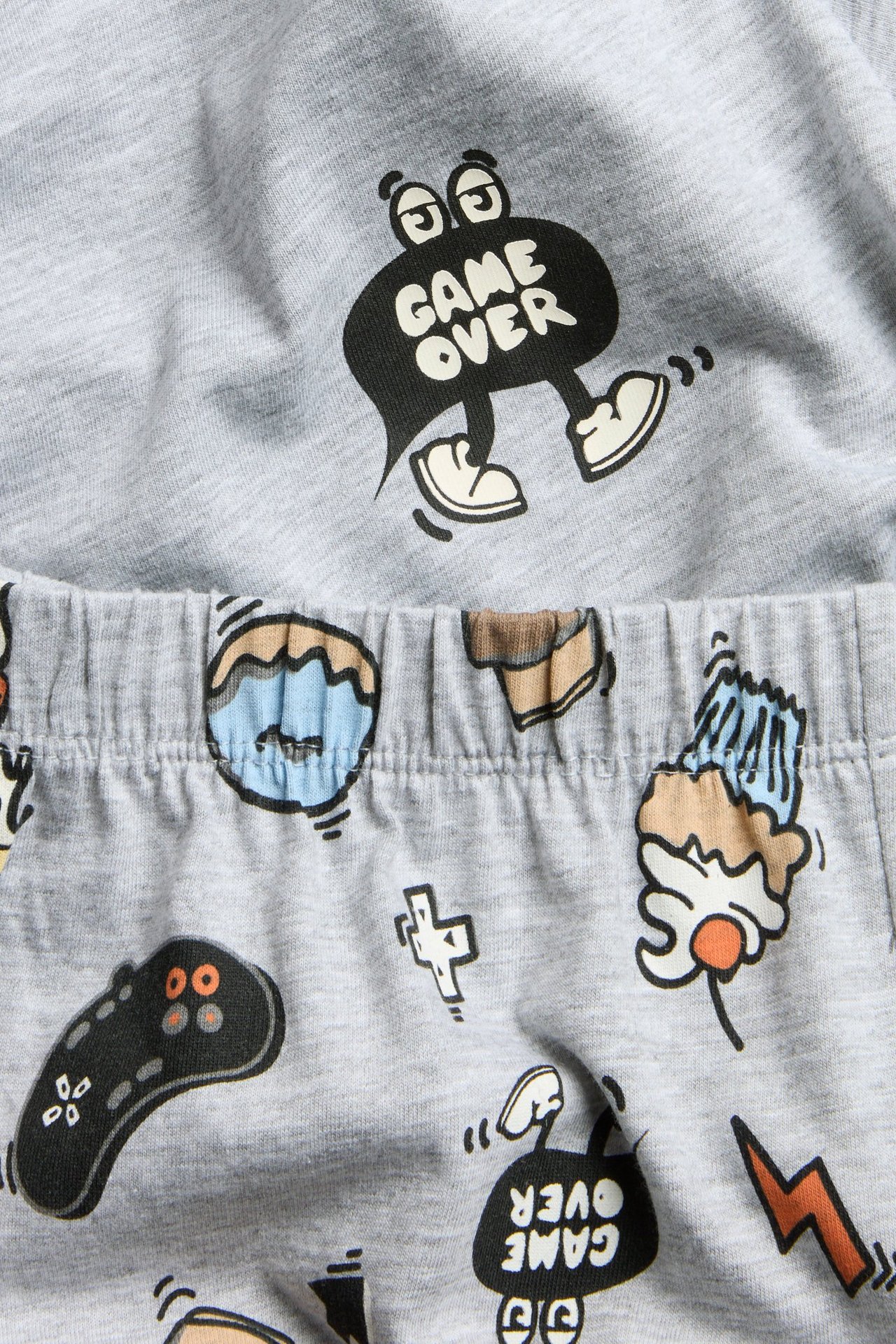 Zbliżenie na szary melanżowy piżamę dziecięcą: top z nadrukiem 'GAME OVER', wzorzyste spodnie z gumką w pasie.