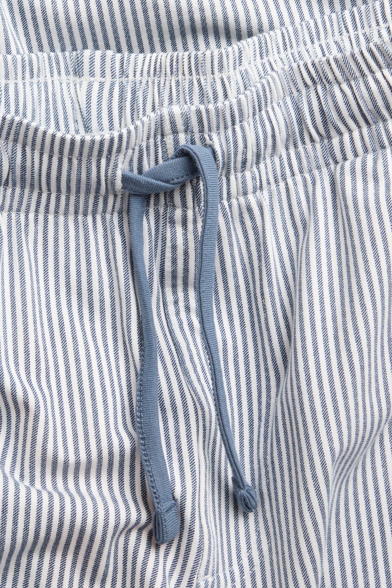 Zbliżenie na granatowo-białe pasiaste spodnie piżamowe z dżerseju z elastyczną talią i niebieskim sznurkiem.