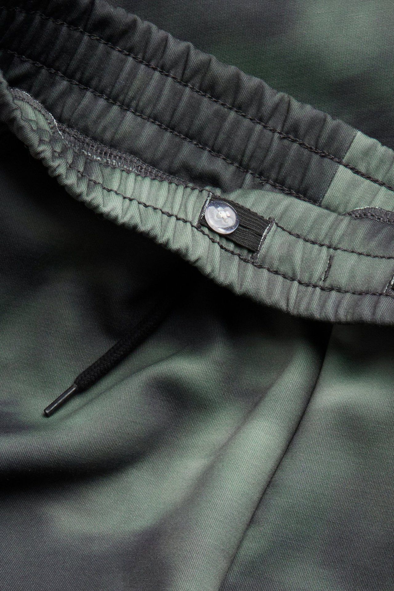 Zbliżenie dziecięcych zielonych wzorzystych spodni dresowych z elastycznym pasem, sznurkiem i regulowanym guzikiem.