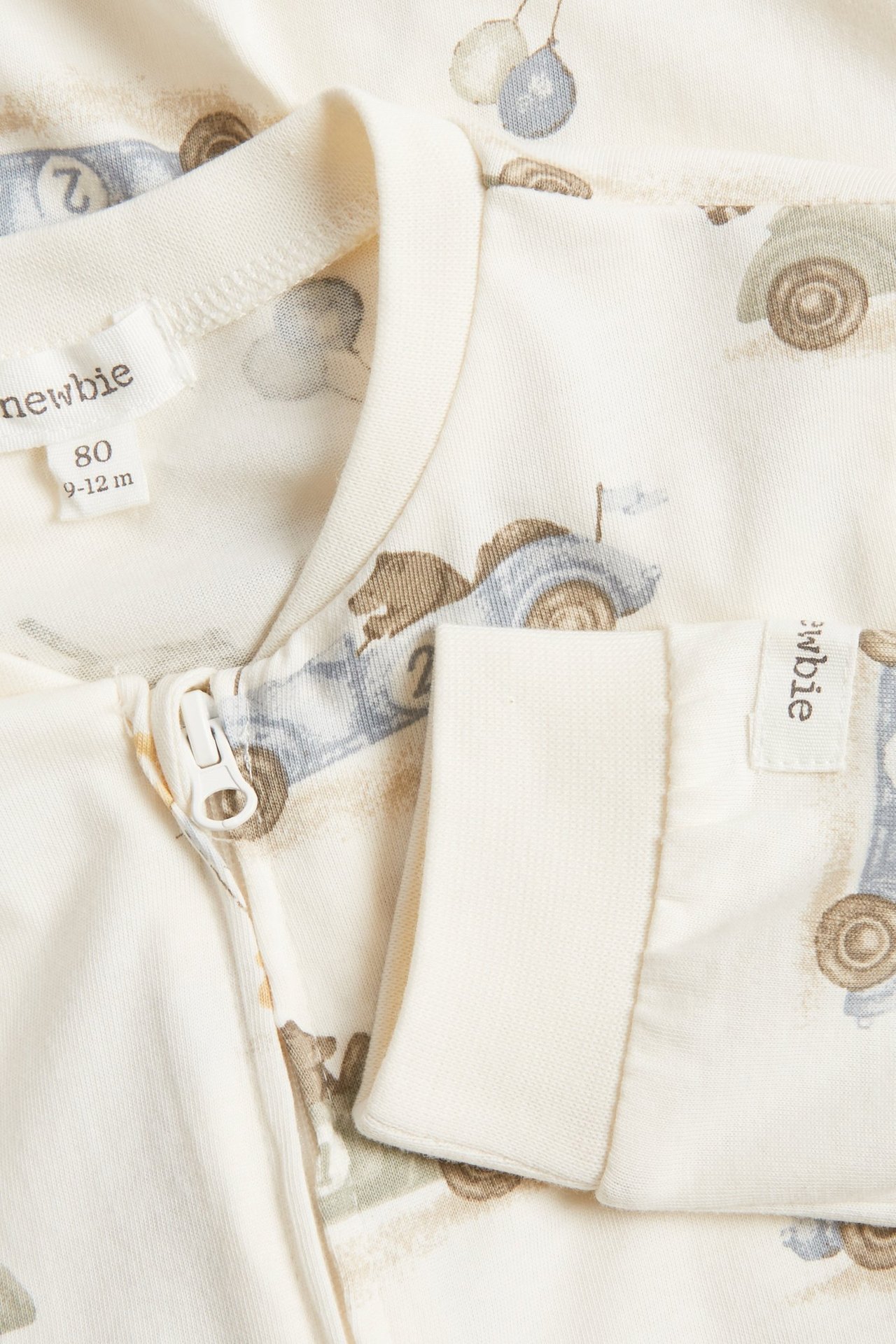 Närbild på offwhite baby pyjamas i mjuk trikå med björn- och bilmönster, tvåvägsdragkedja.