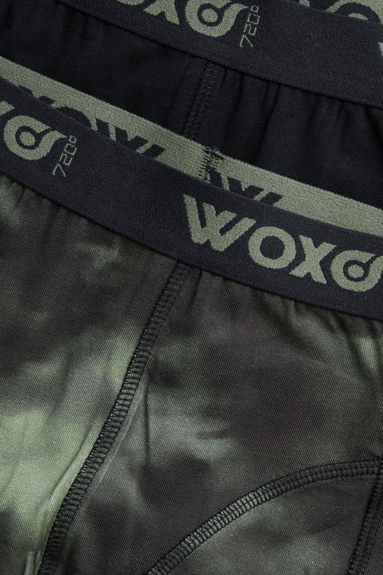 Zbliżenie na dwie pary bokserek dziecięcych: jedne zielone we wzory, drugie czarne, z gumką w pasie.