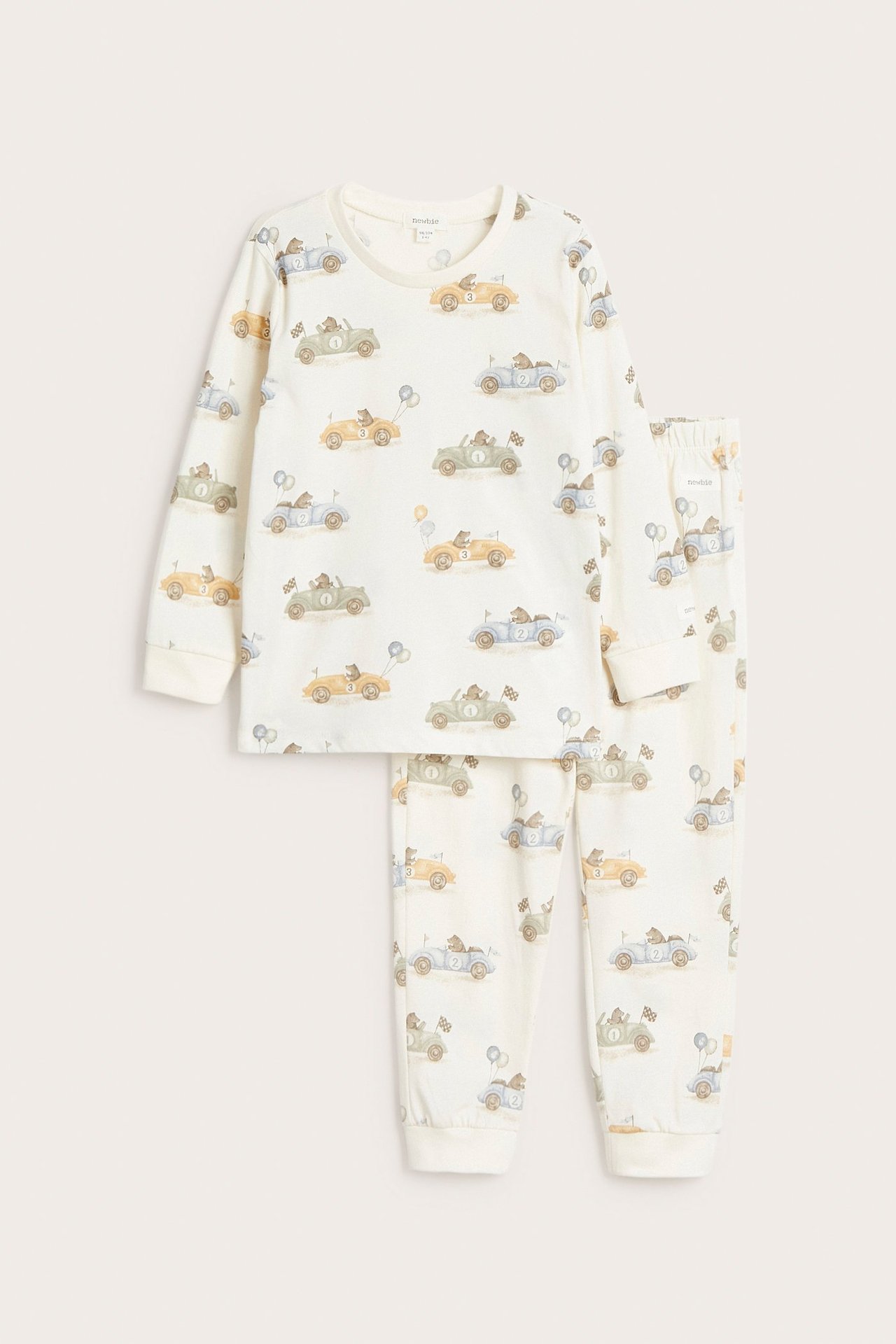 Edestä: Luonnonvalkoinen kaksiosainen lasten puuvillapyjama, jossa on kauttaaltaan karhu- ja autoaiheinen kuvio.