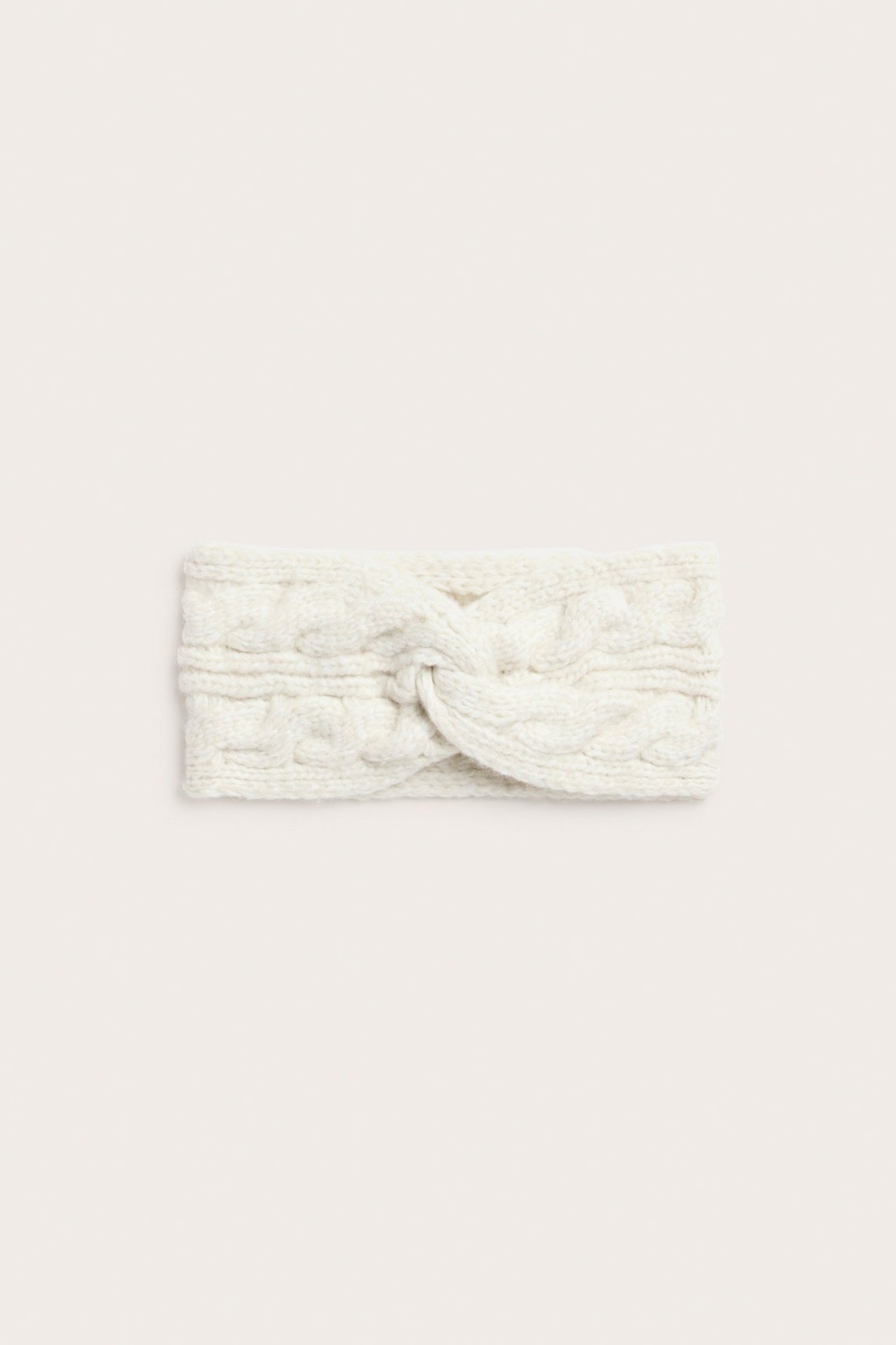 Lähikuva edestä, luonnonvalkoinen palmikkoneulottu panta, jossa kierretty yksityiskohta.