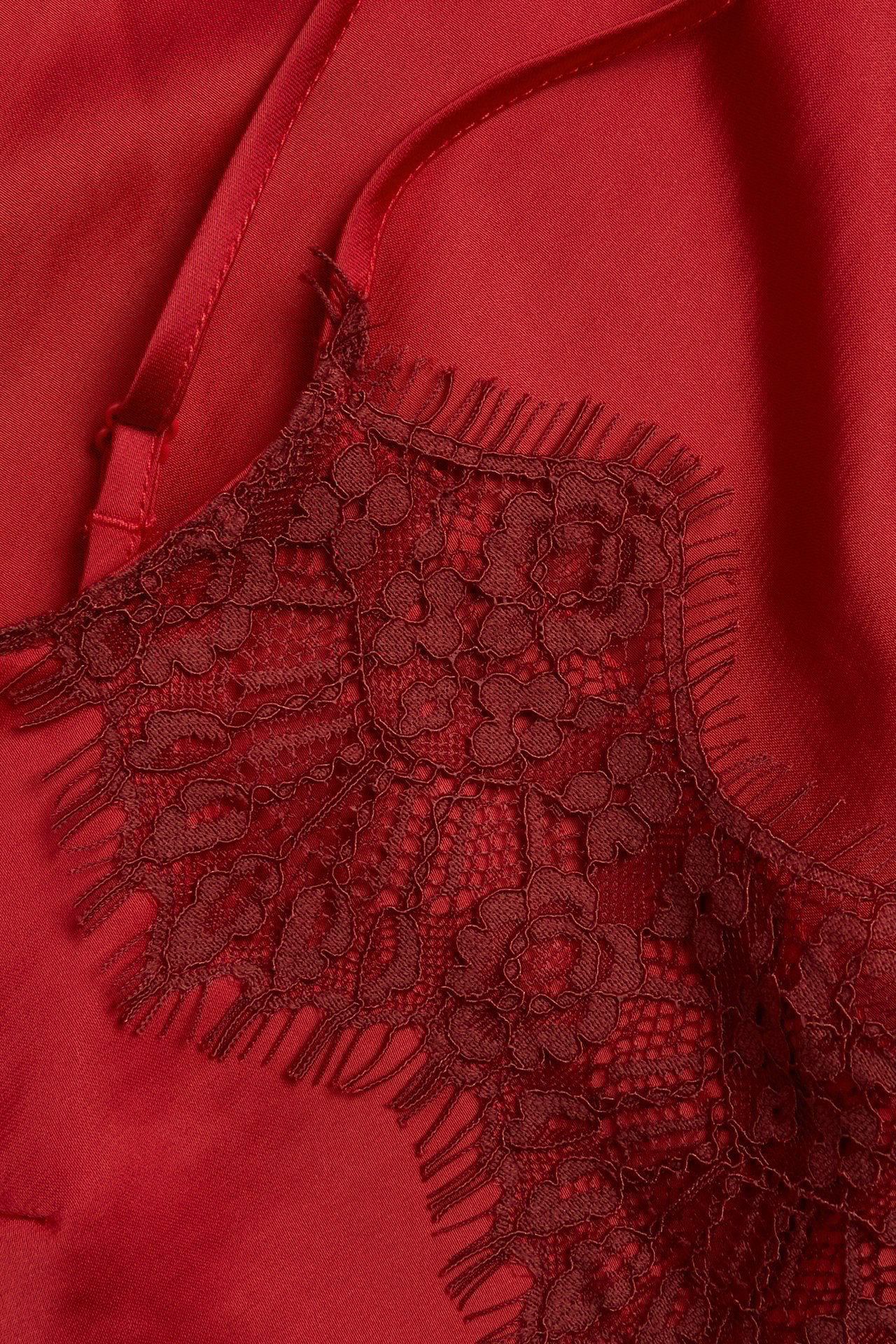 Zbliżenie czerwonego satynowego topu z delikatną koronkową lamówką i regulowanymi ramiączkami.