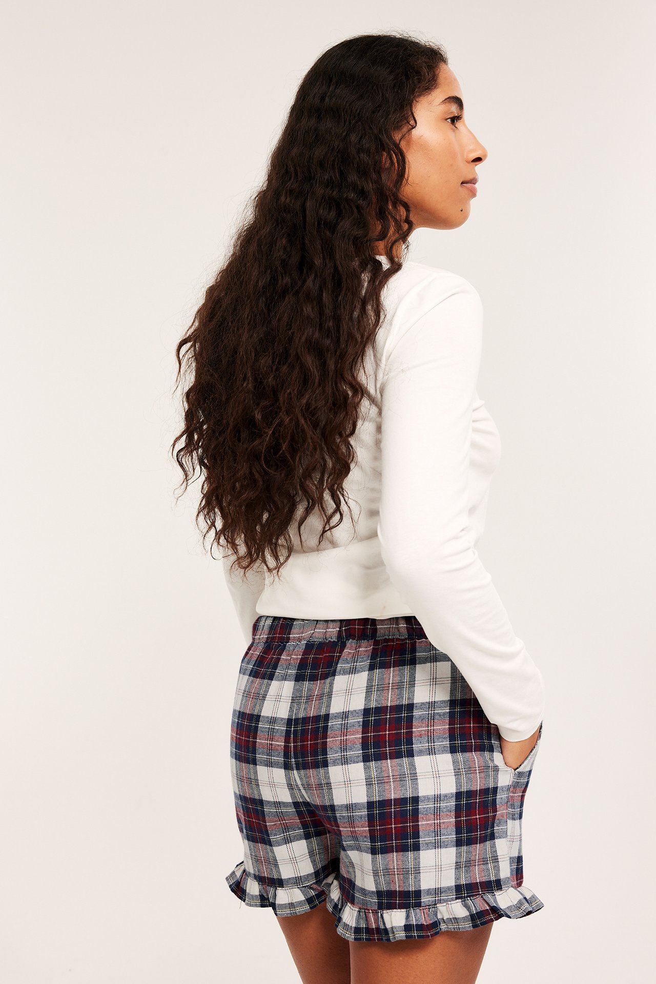 Nainen valkoisessa yläosassa ja ruudulliset sininen, punainen, valkoinen pyjamashortsit röyhelöreunuksella.