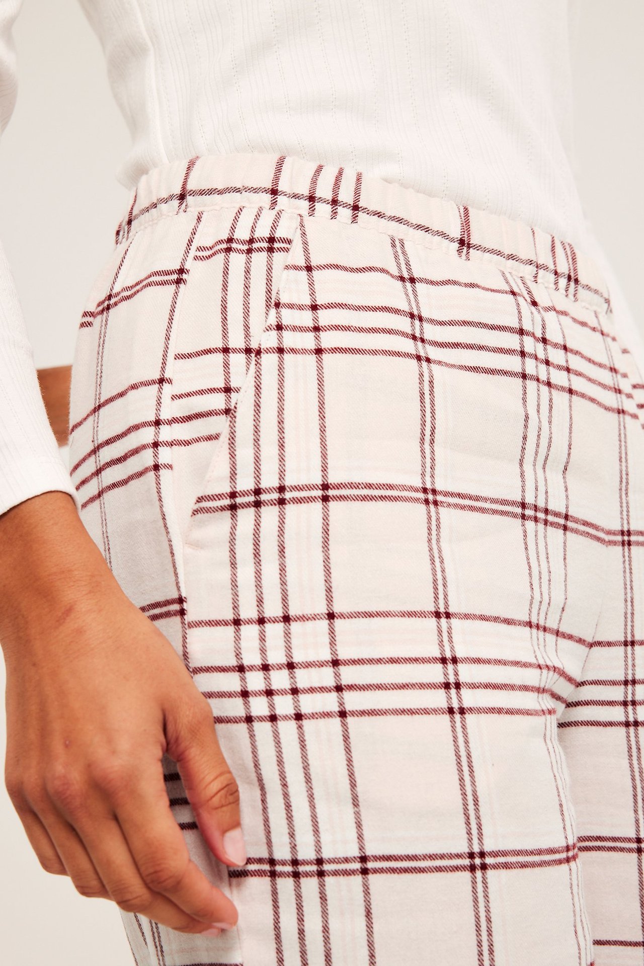 Lähikuva: Nainen yllään vaaleanpunaiset ruudulliset flanellipyjamahousut, joustovyötärö, sivutaskut, valkoinen ribbitoppi.