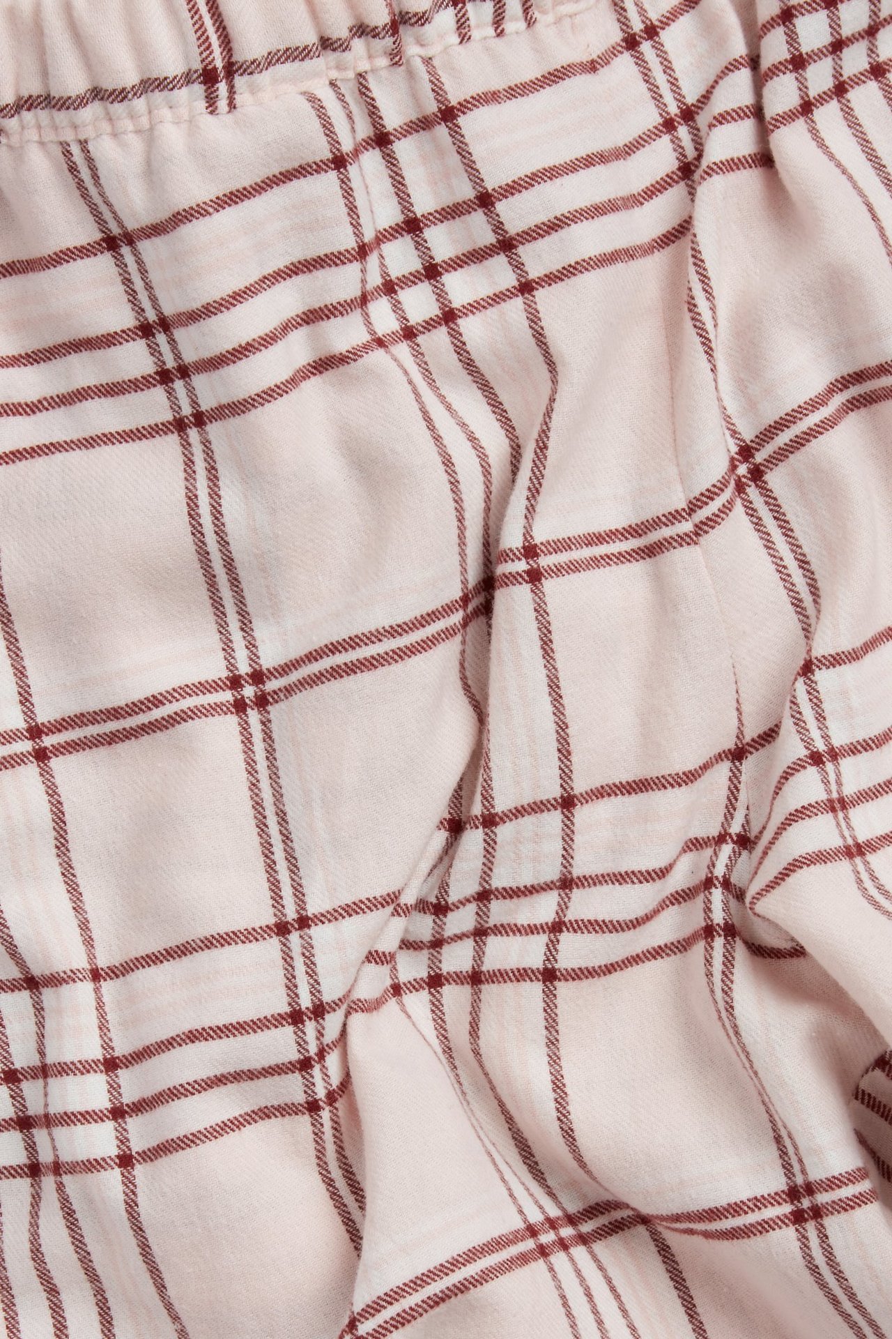 Nærbilde av lyserosa flanellpyjamasbukser med vinrødt rutete mønster og strikk i midjen.