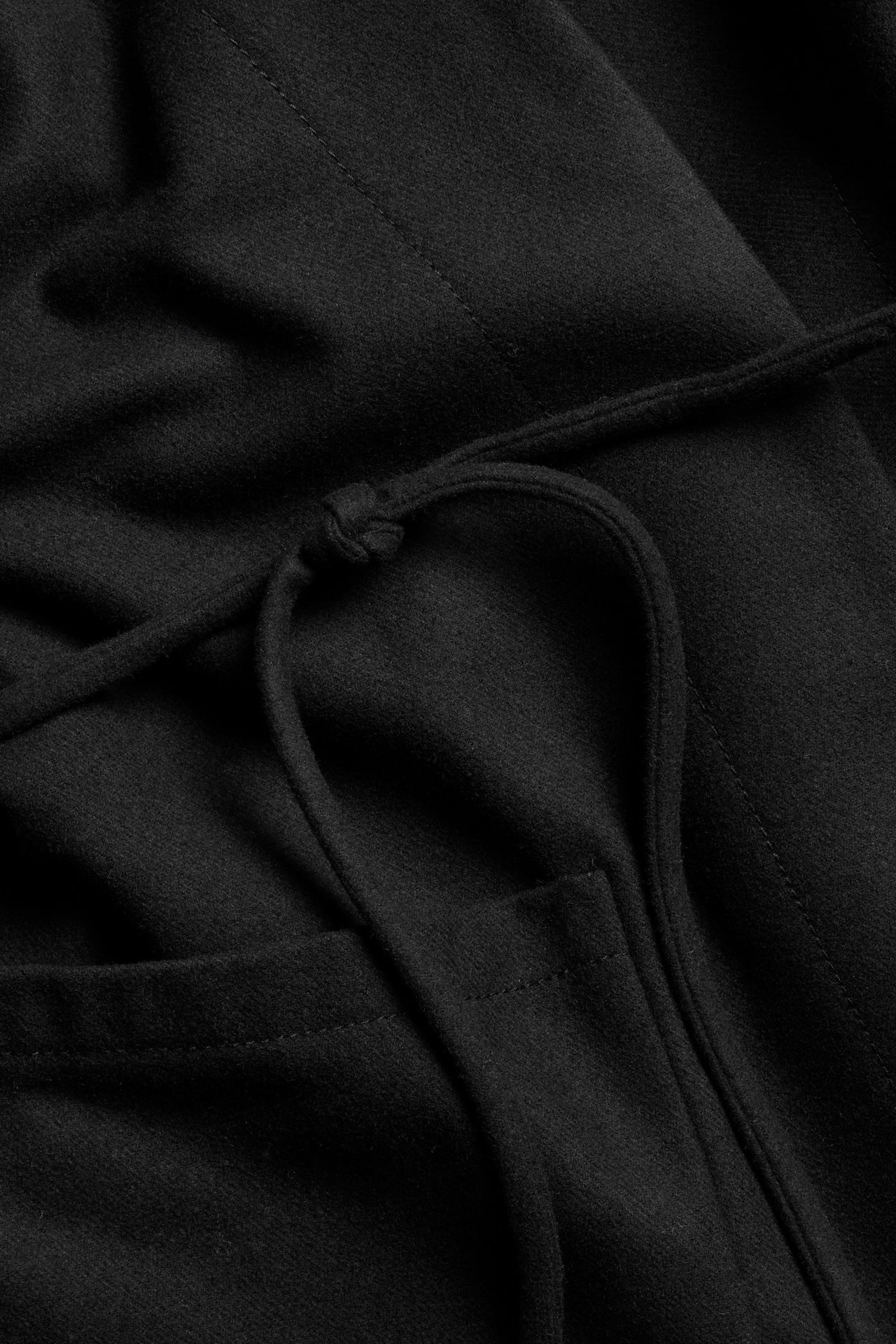 Zbliżenie czarnej kurtki z mieszanki wełny z wiązanym paskiem i kieszenią.