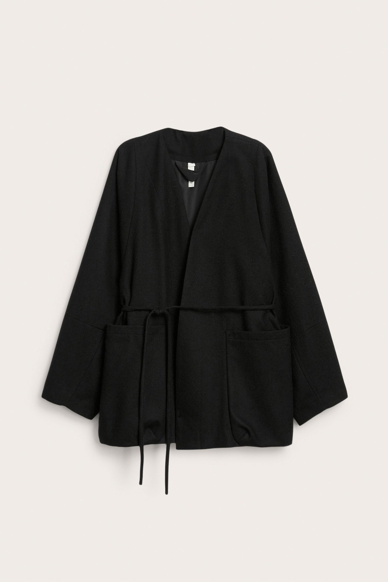 Edestäpäin musta villasekoitejakku, jossa kaulukseton malli, solmittava vyö ja kaksi etutaskua.