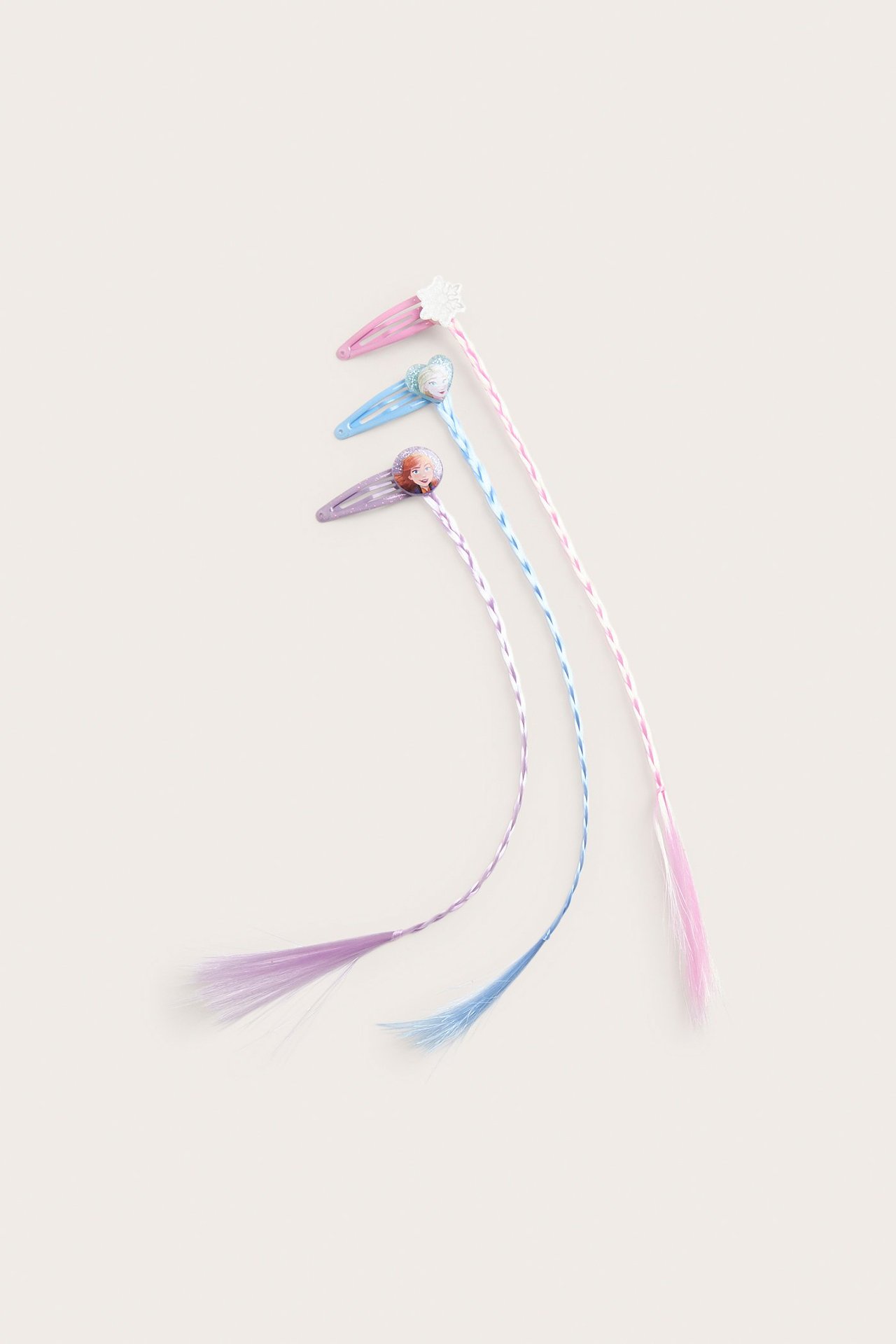 Widok z góry na trzy spinki Frozen z warkoczami: różowa płatek śniegu, jasnoniebieska Elsa, fioletowa Anna.