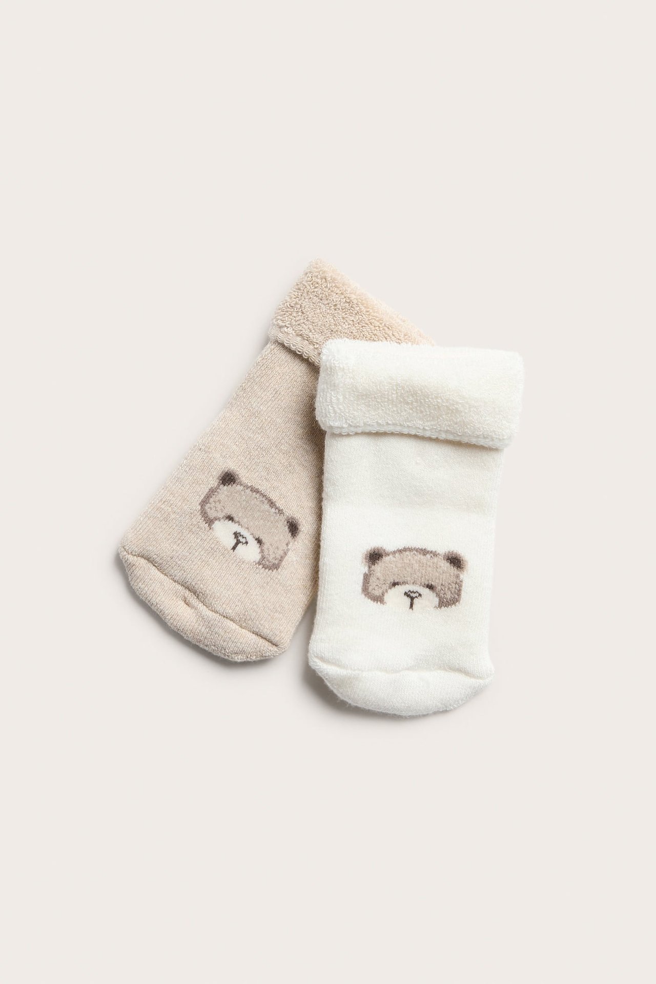 Ovenfra: to babyfrottersokker, en offwhite, en lys beige, begge med nedbrettet kant og bamsemønster.