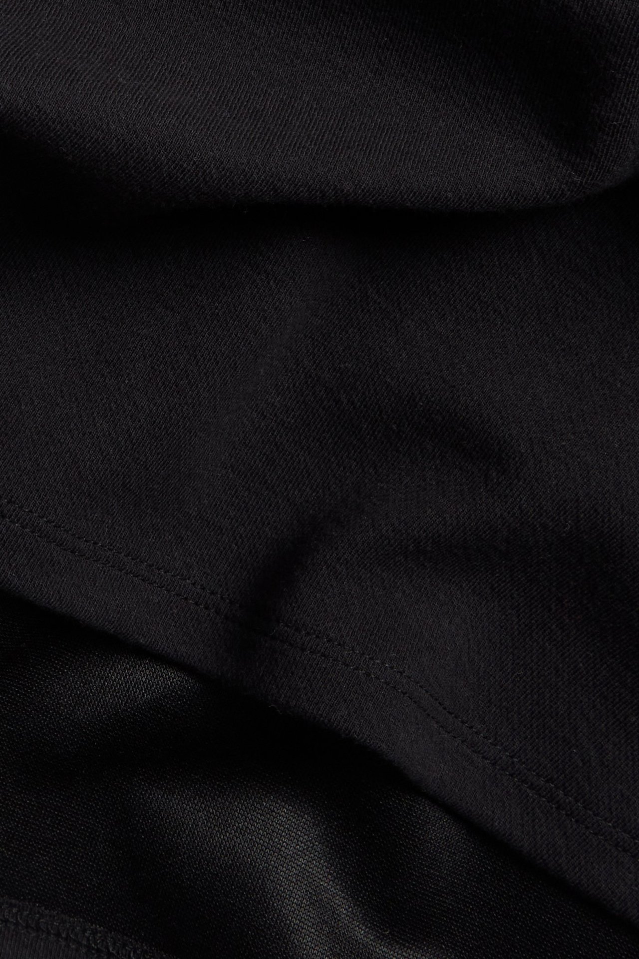 Zbliżenie czarnego, jednolitego materiału spódnicy z bawełny i poliestru, z widocznymi szwami.