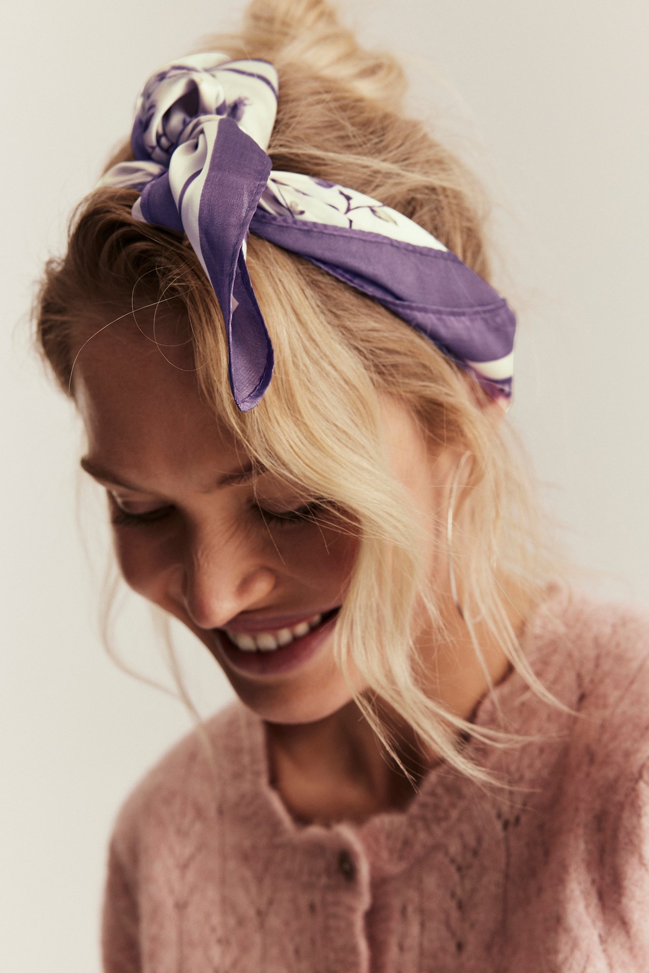 Nærbilde av kvinne med lys lilla blomstret skjerf som hårband og rosa cardigan.