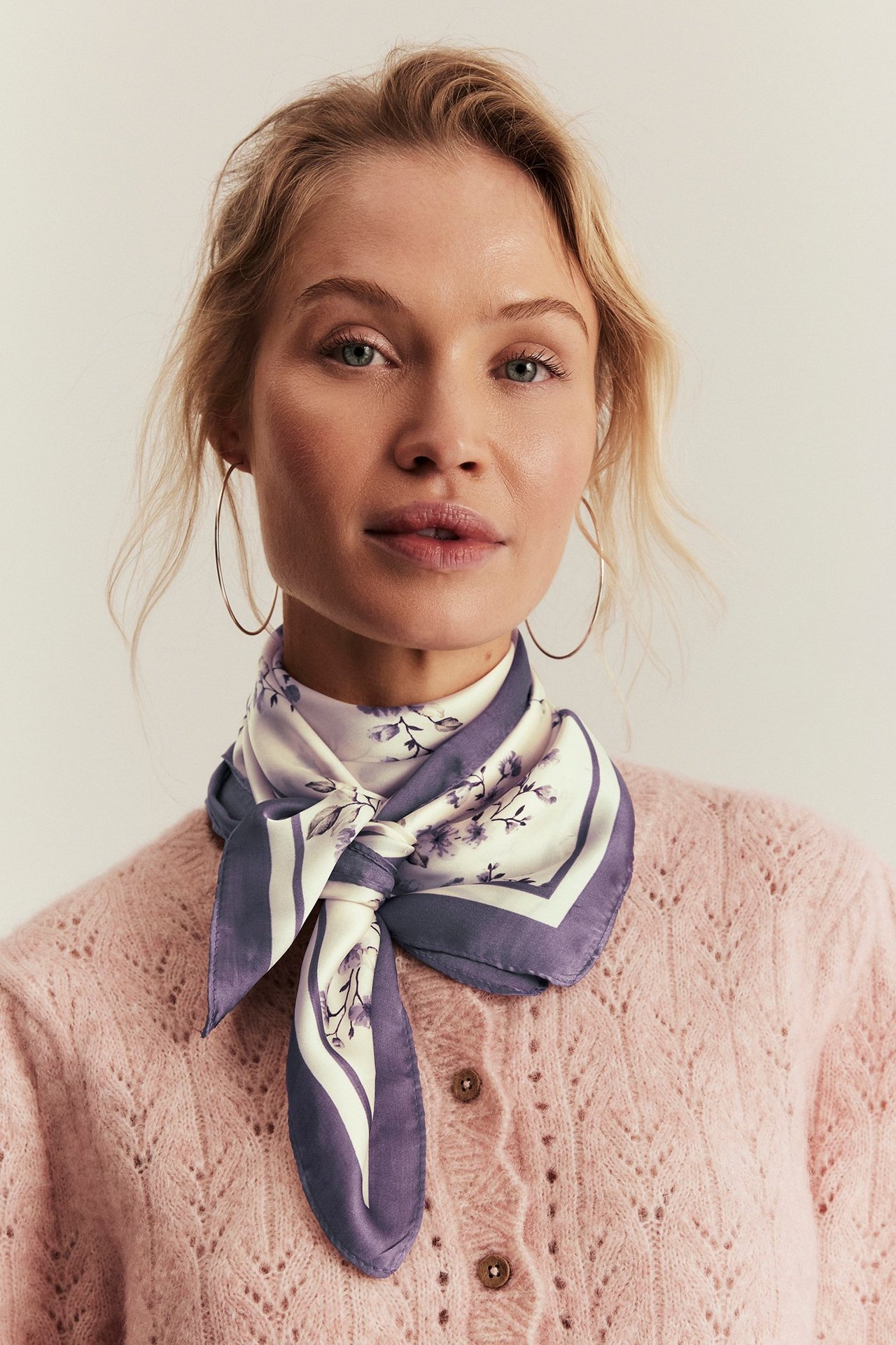 Widok z przodu, zbliżenie: kobieta w biało-liliowej, kwiecistej apaszce poliestrowej na różowym kardiganie.