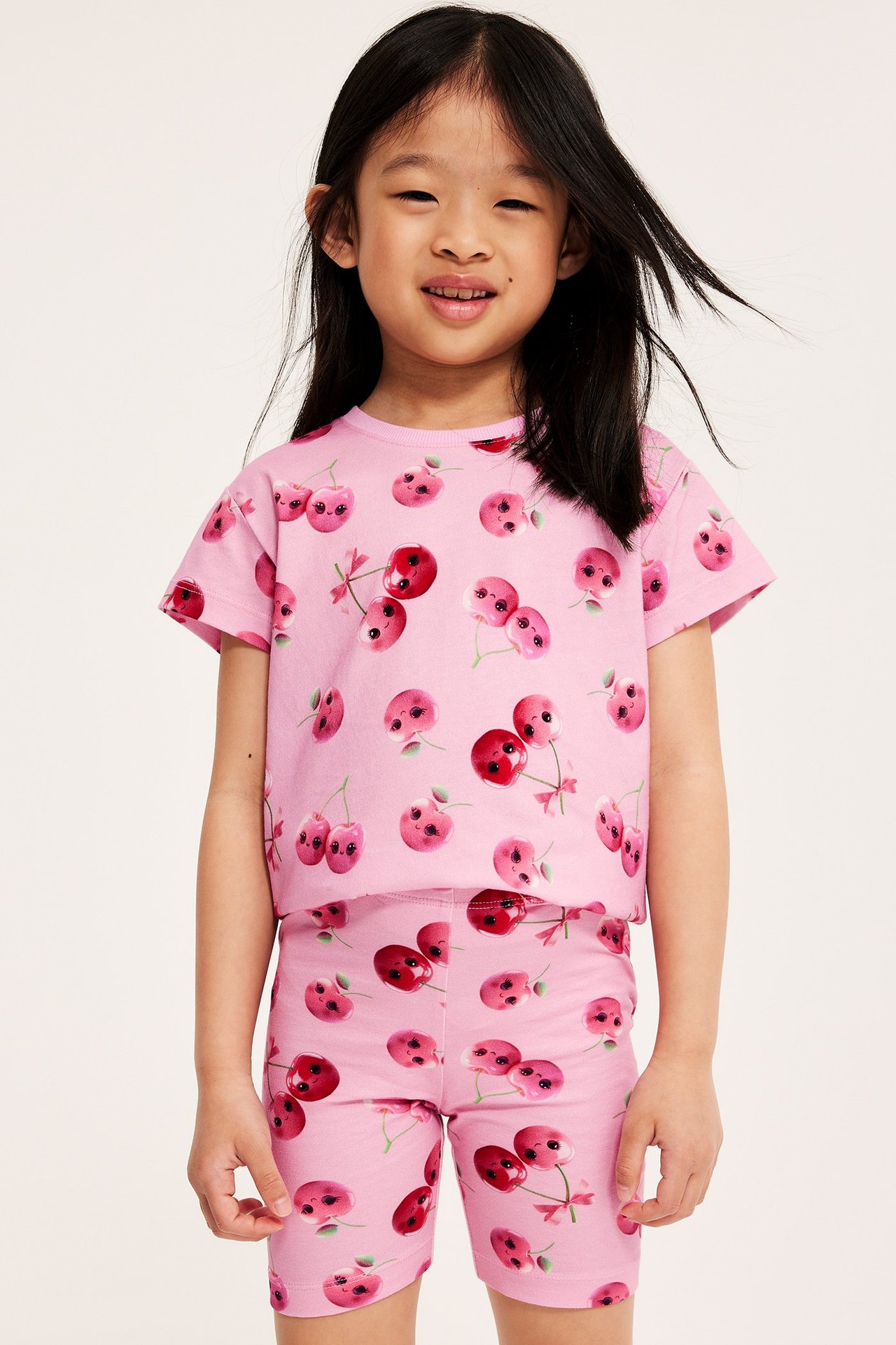 Framifrån: ett barn i rosa cykelbyxor och matchande t-shirt med körsbärsmönster.