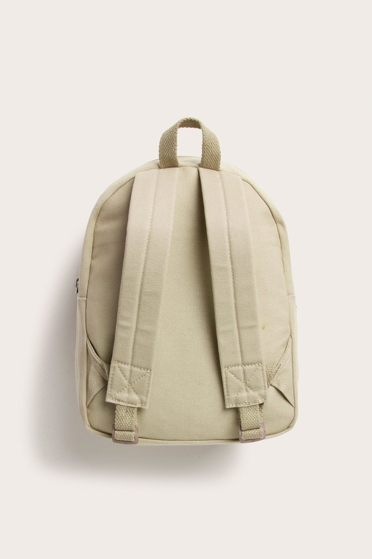 Bakfra av en beige ryggsekk i bomullscanvas med justerbare skulderstropper og et håndtak.