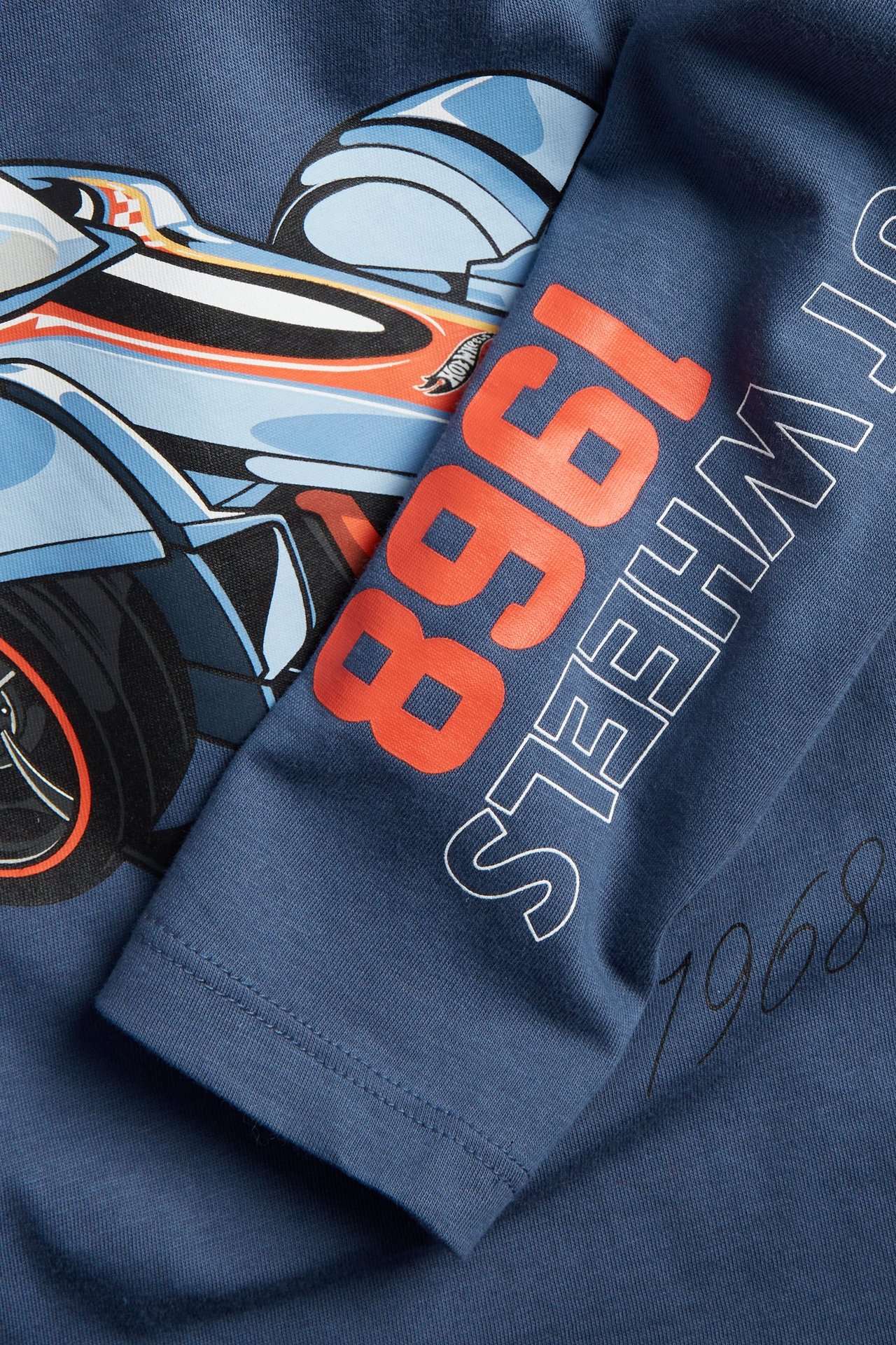 Närbild av en blå långärmad t-shirt i bomull för barn med Hot Wheels bil-tryck och text.