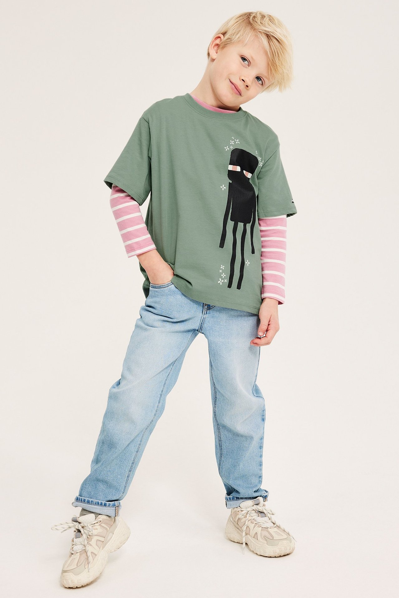 Framifrån: Pojke i grön Minecraft Enderman T-shirt, rosa randig topp, ljusblåa jeans och beiga sneakers.