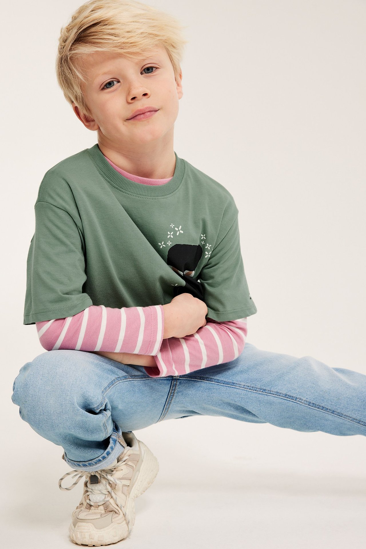 Chłopiec z przodu: zielona koszulka Minecraft Enderman na różowej bluzce w paski, jasnoniebieskie jeansy, beżowe sneakersy.