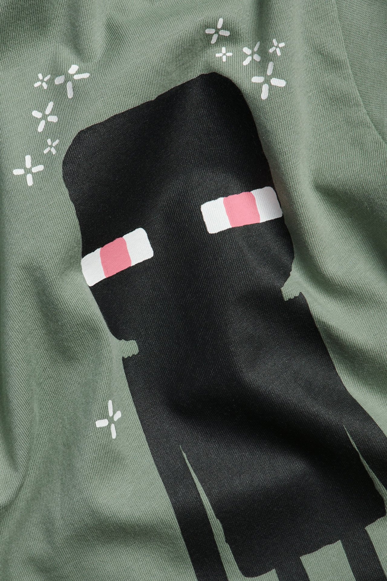 Närbild på en grön bomulls-t-shirt för barn med svart Minecraft Enderman-tryck och vita stjärndetaljer.