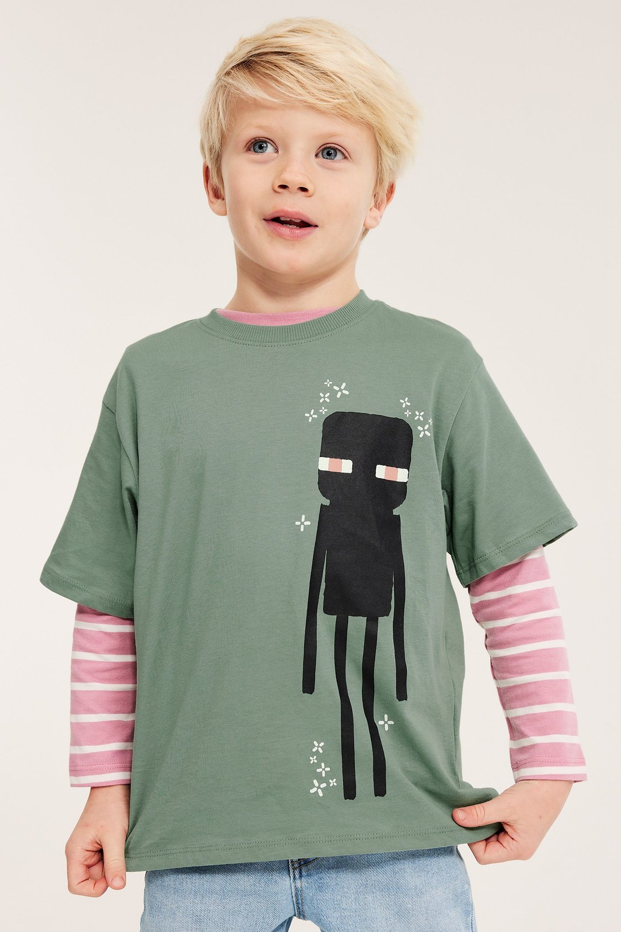 Przód: Dziecko w zielonej koszulce T-shirt Minecraft Enderman, na różowej koszulce w paski, niebieskie jeansy.