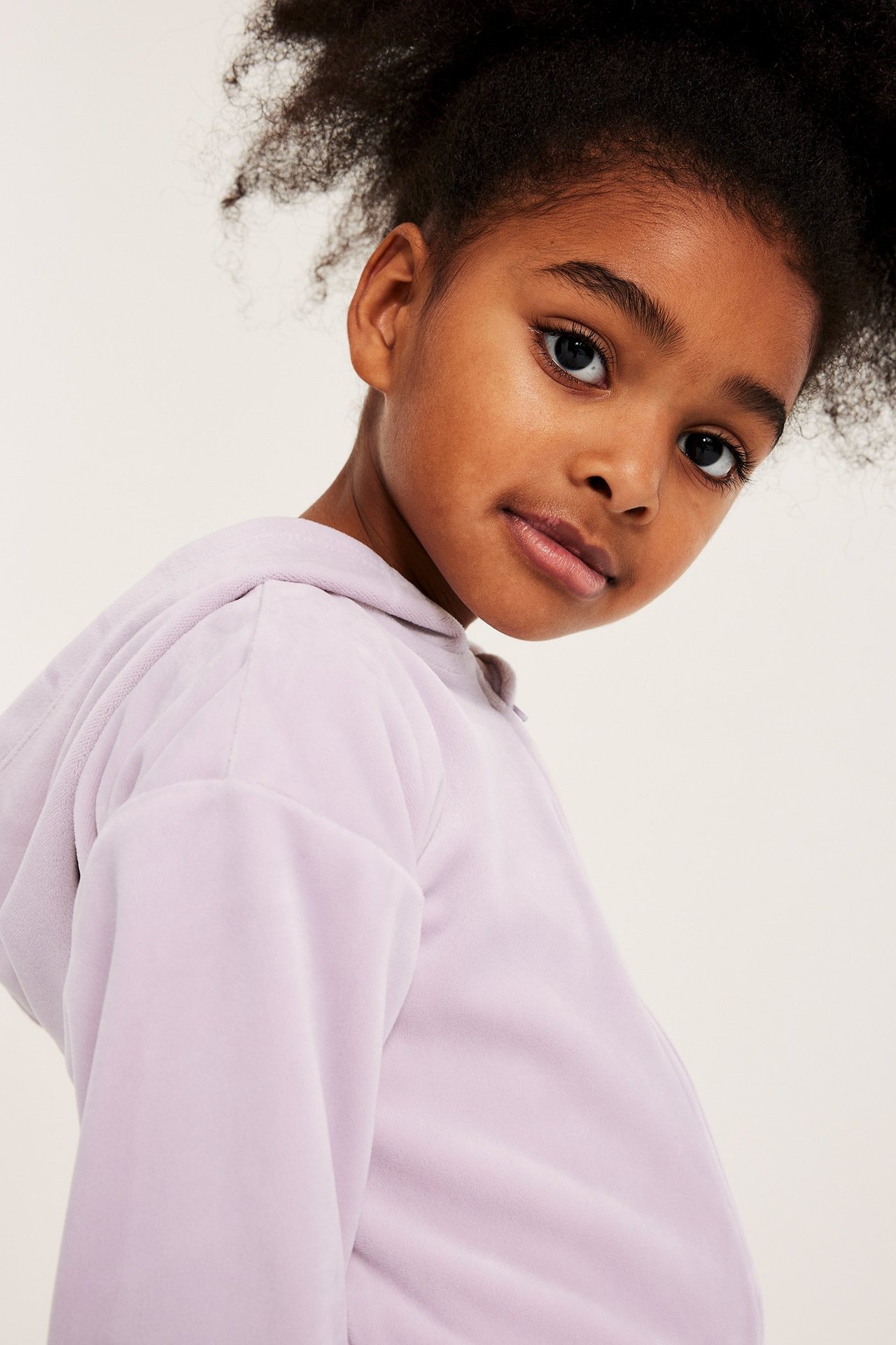 Lähikuva lapsesta, joka käyttää yksiväristä vaaleanlilaa veluurihupparia.
