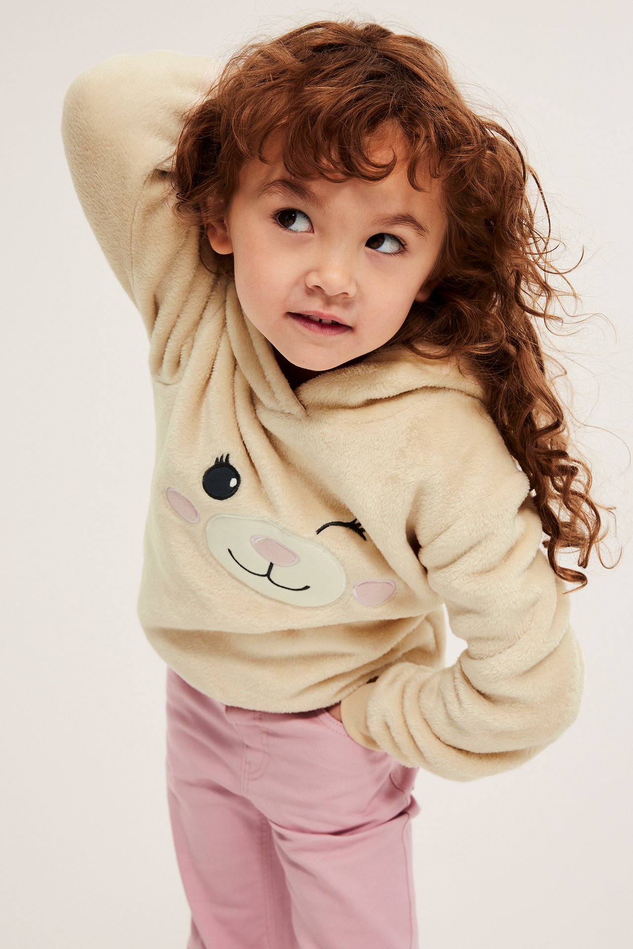 Edestäpäin: lapsi yllään vaaleanbeige pörröhuppari, jossa eläinkuvio, ja vaaleanpunaiset housut.