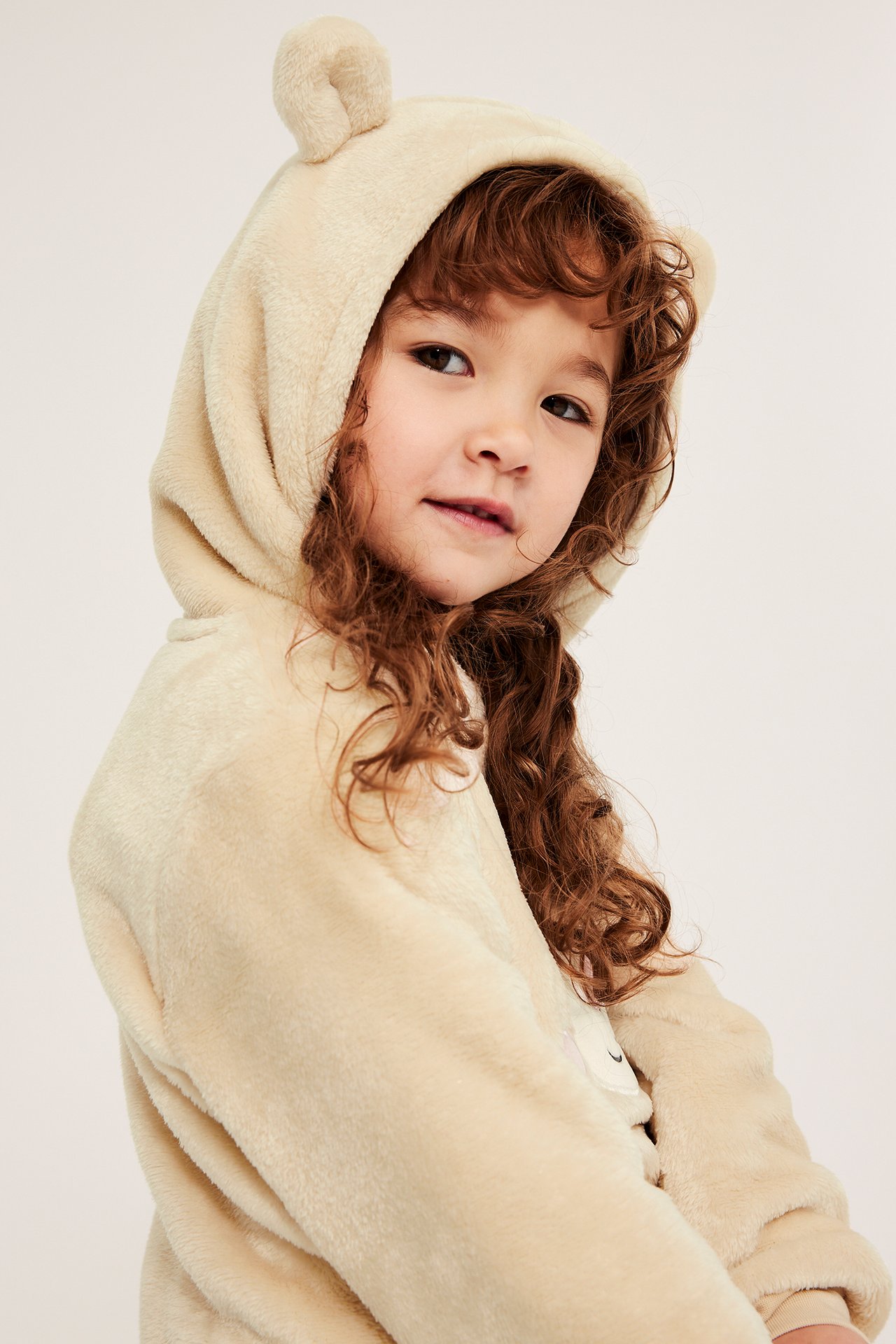 Lähikuva edestä: lapsi yllään vaaleanbeige pörröinen huppari, jossa pienet korvat hupussa.