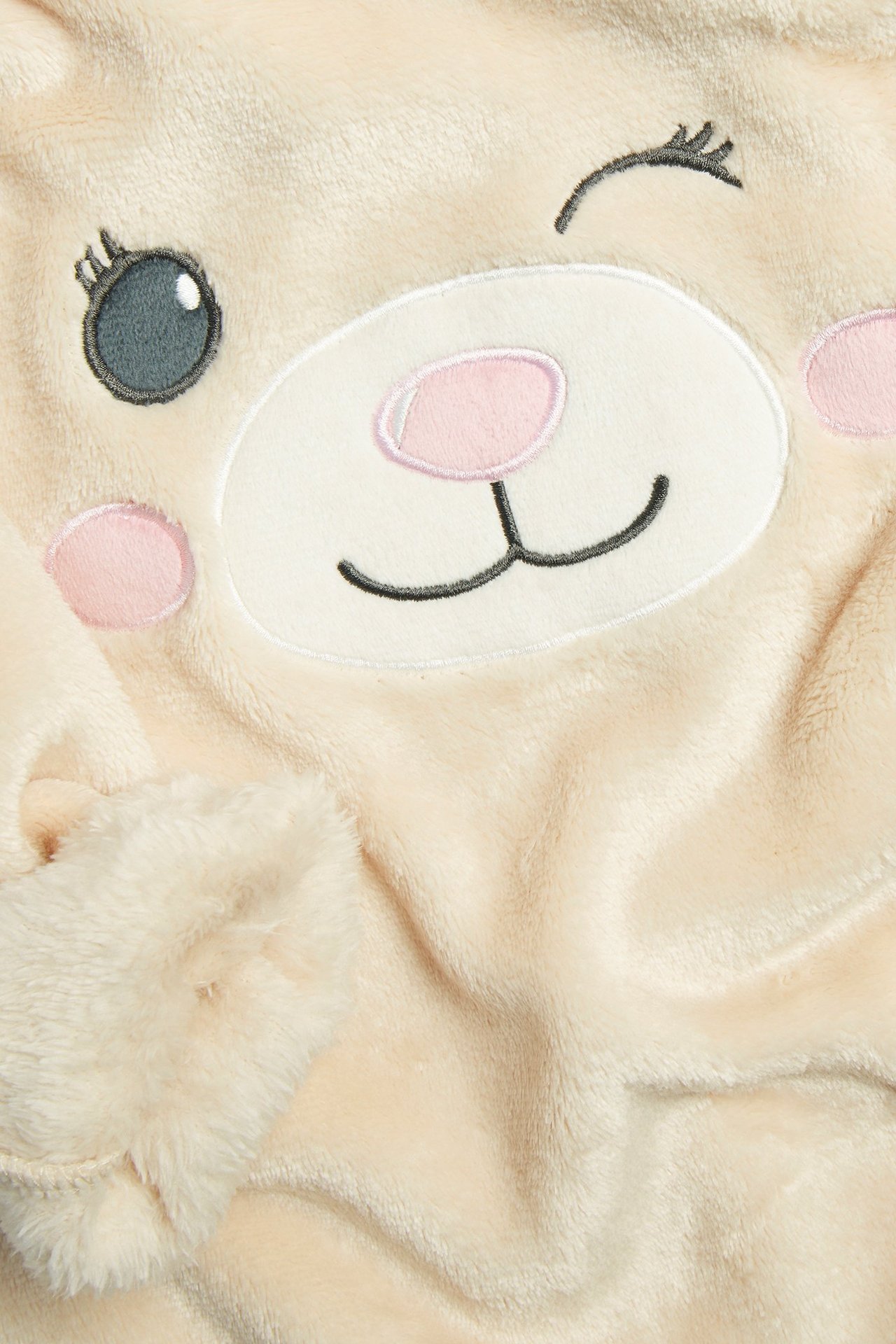 Zbliżenie jasnobeżowej puszystej bluzy dziecięcej z haftowanym wzorem mrugającej buzi zwierzęcia i puszystym rękawem.