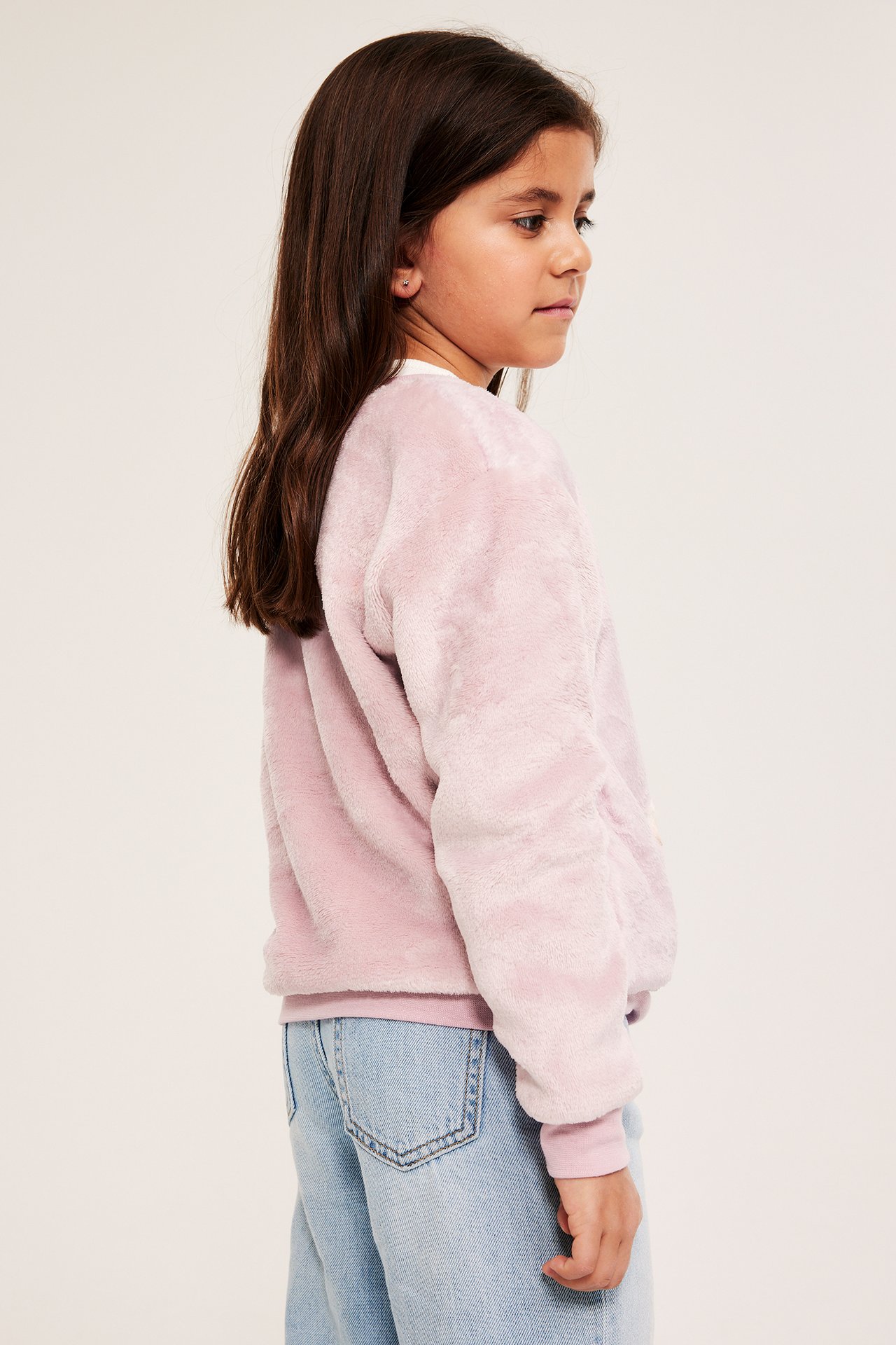 Sivukuva lapsesta pörröisessä vaaleanpunaisessa polyestercollegepaidassa vaaleansinisten farkkujen päällä.