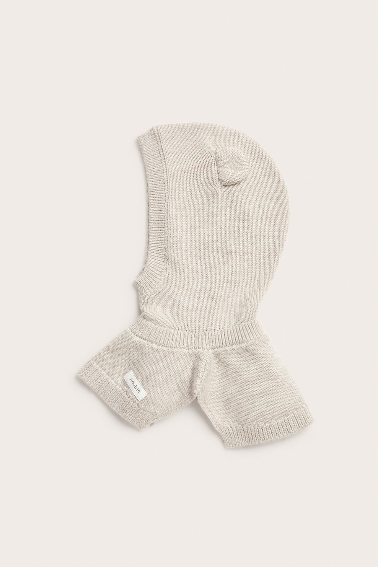 Forfra, lys beige strikket babybalaklava med små ører og en etikett.