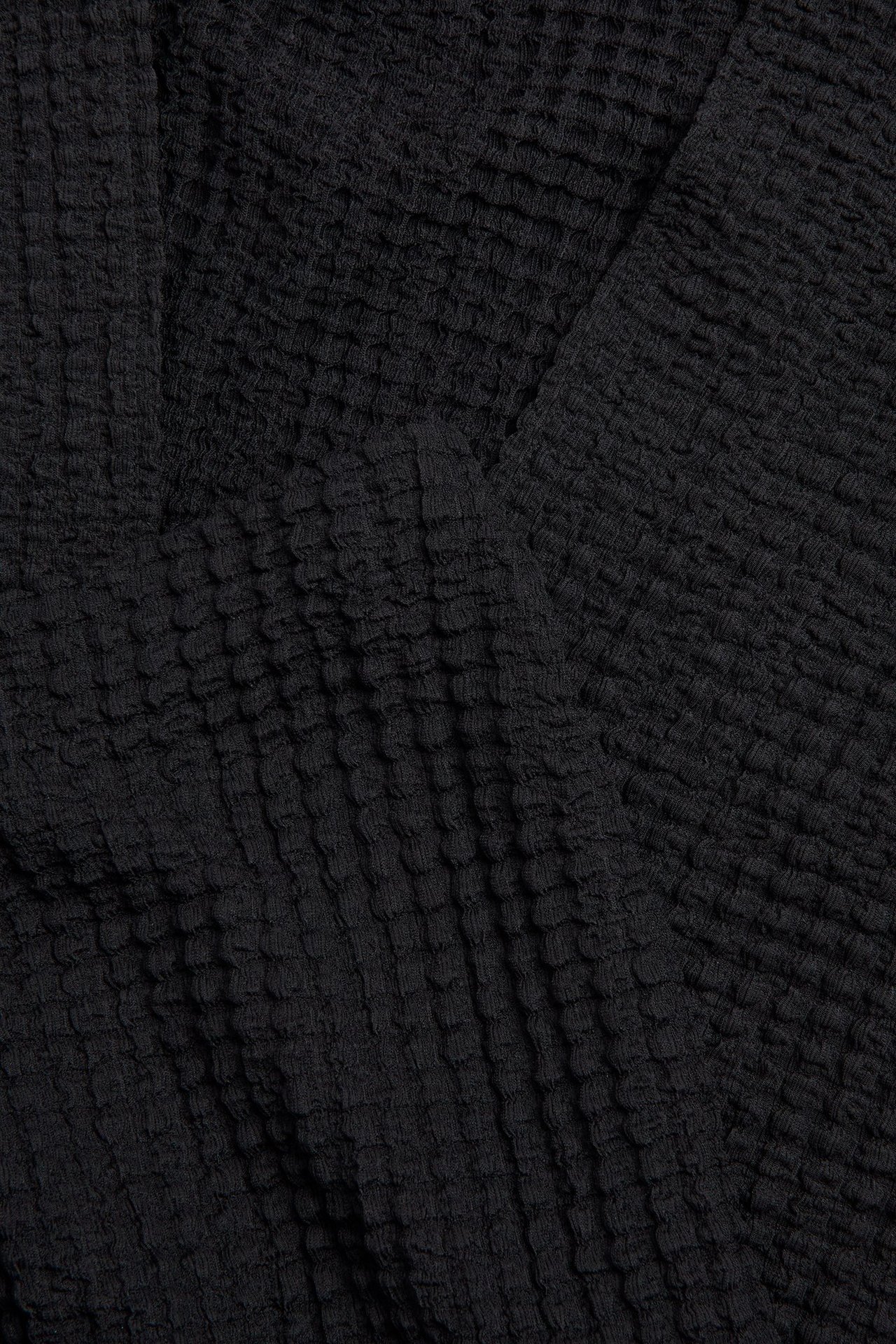 Zbliżenie na czarny, strukturalny materiał długiej spódnicy, ukazujące jego teksturowaną, jednolitą powierzchnię.