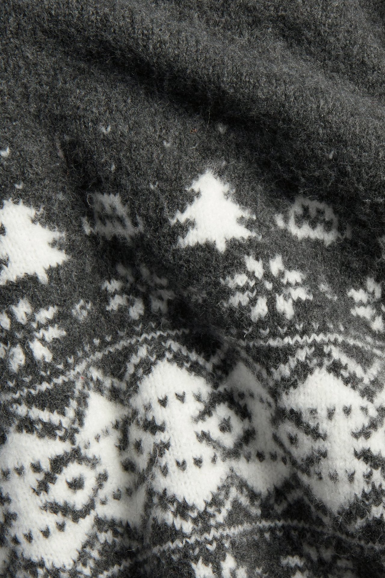 Lähikuva tummanharmaasta neulotusta joulupaidasta, jossa valkoisia jacquardkuvioita, kuusia ja lumihiutaleita.