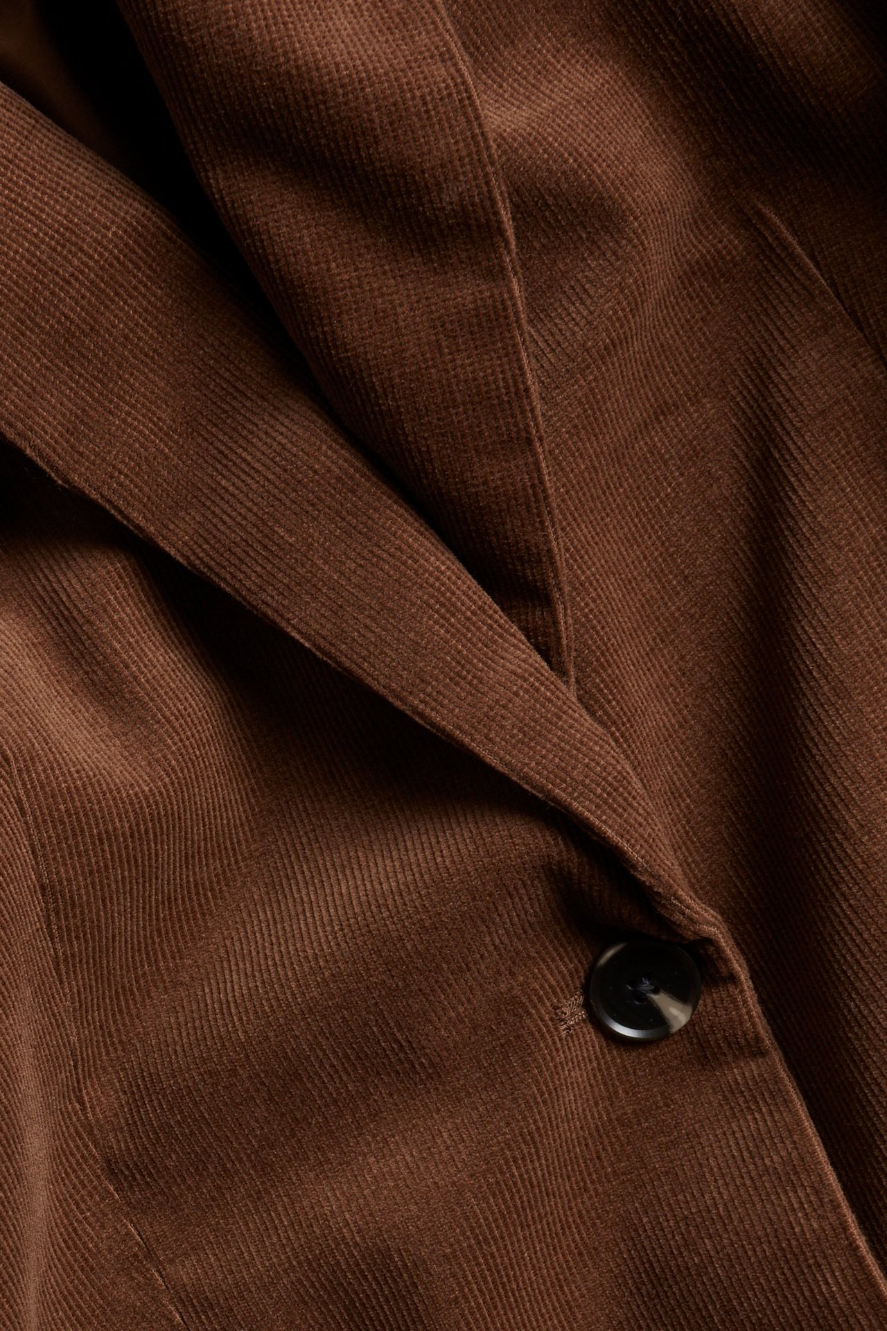 Zbliżenie brązowej sztruksowej marynarki z ciemnym guzikiem i detalem klapy.