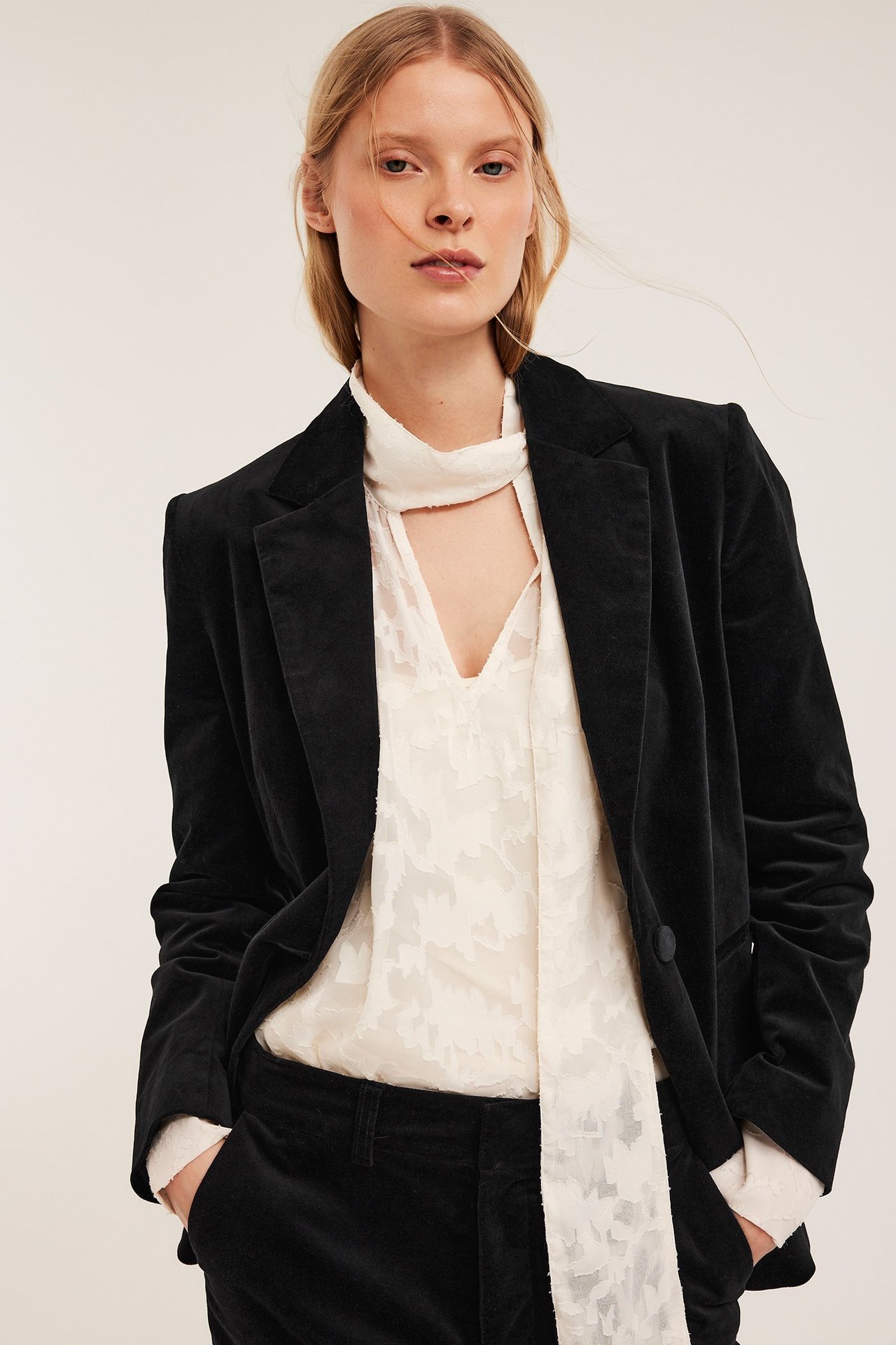 Edestä: Nainen mustassa samettibleiserissä, vaaleabeigessä solmupaidassa ja samettihousuissa.