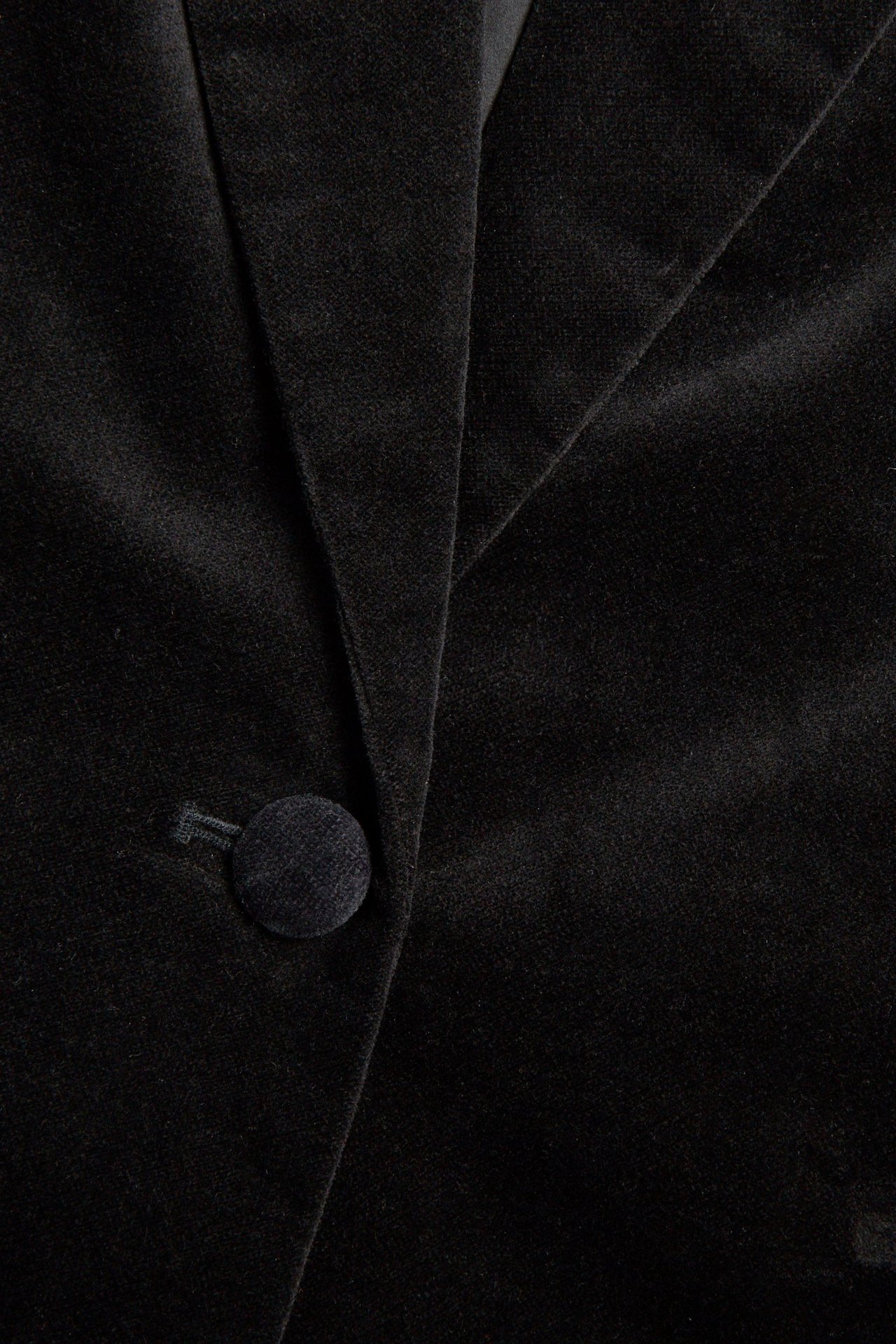 Zbliżenie na czarny aksamitny blezer z zapięciem na jeden guzik i detalami klap.