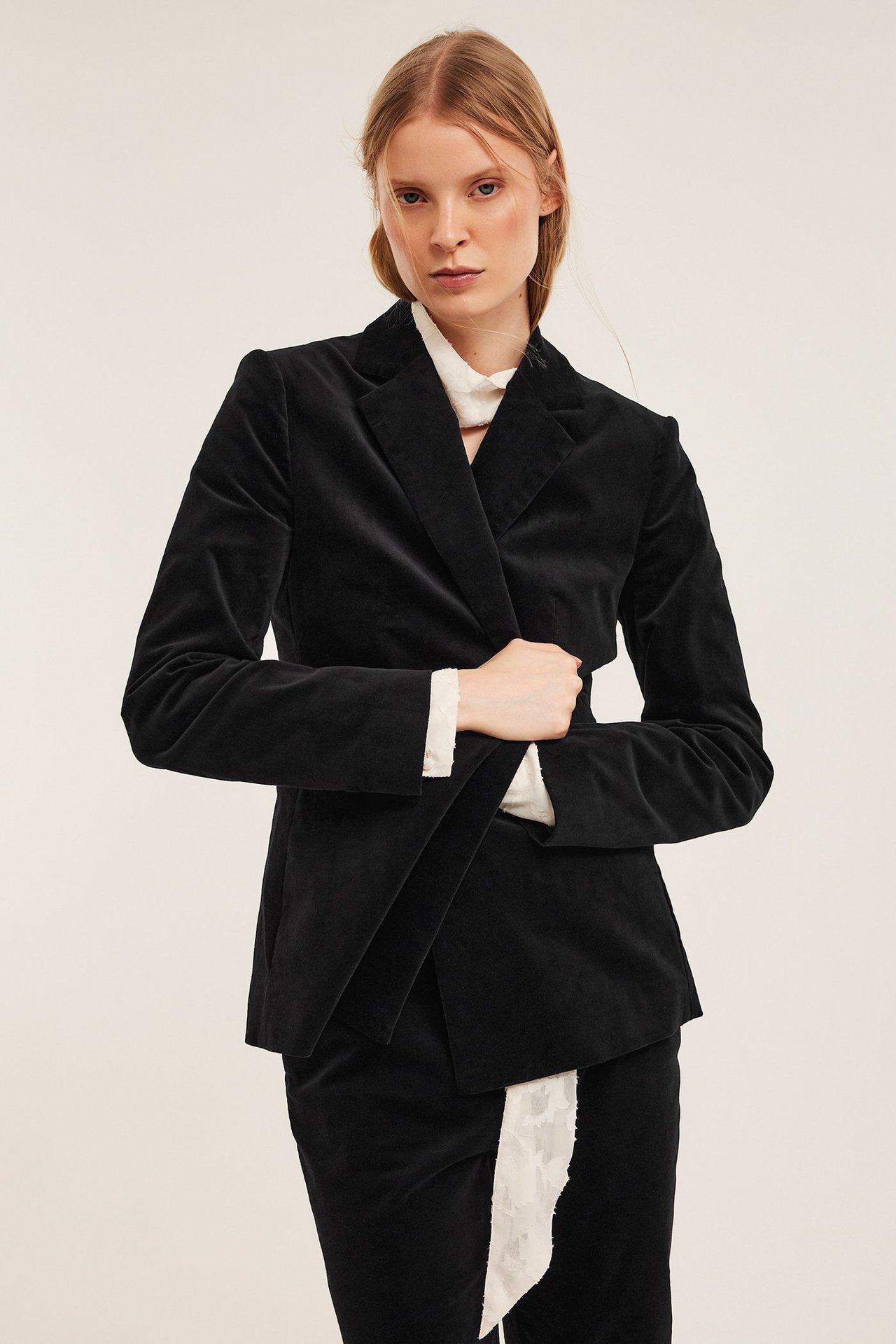 Kobieta w czarnej aksamitnej marynarce, białej wzorzystej bluzce i pasującej spódnicy.