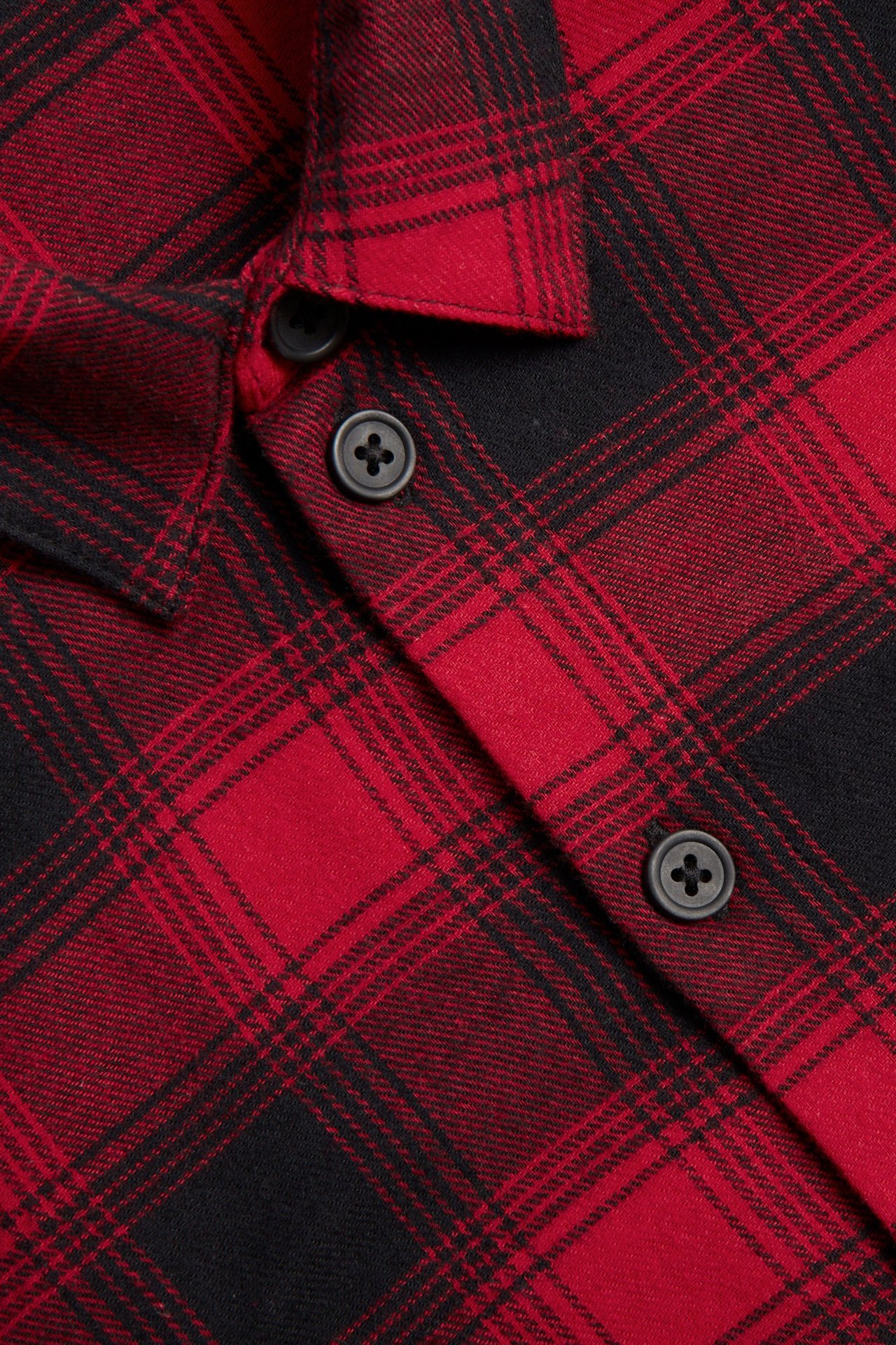 Zbliżenie na czerwoną i czarną kraciastą koszulę flanelową z bawełny z ciemnymi guzikami.