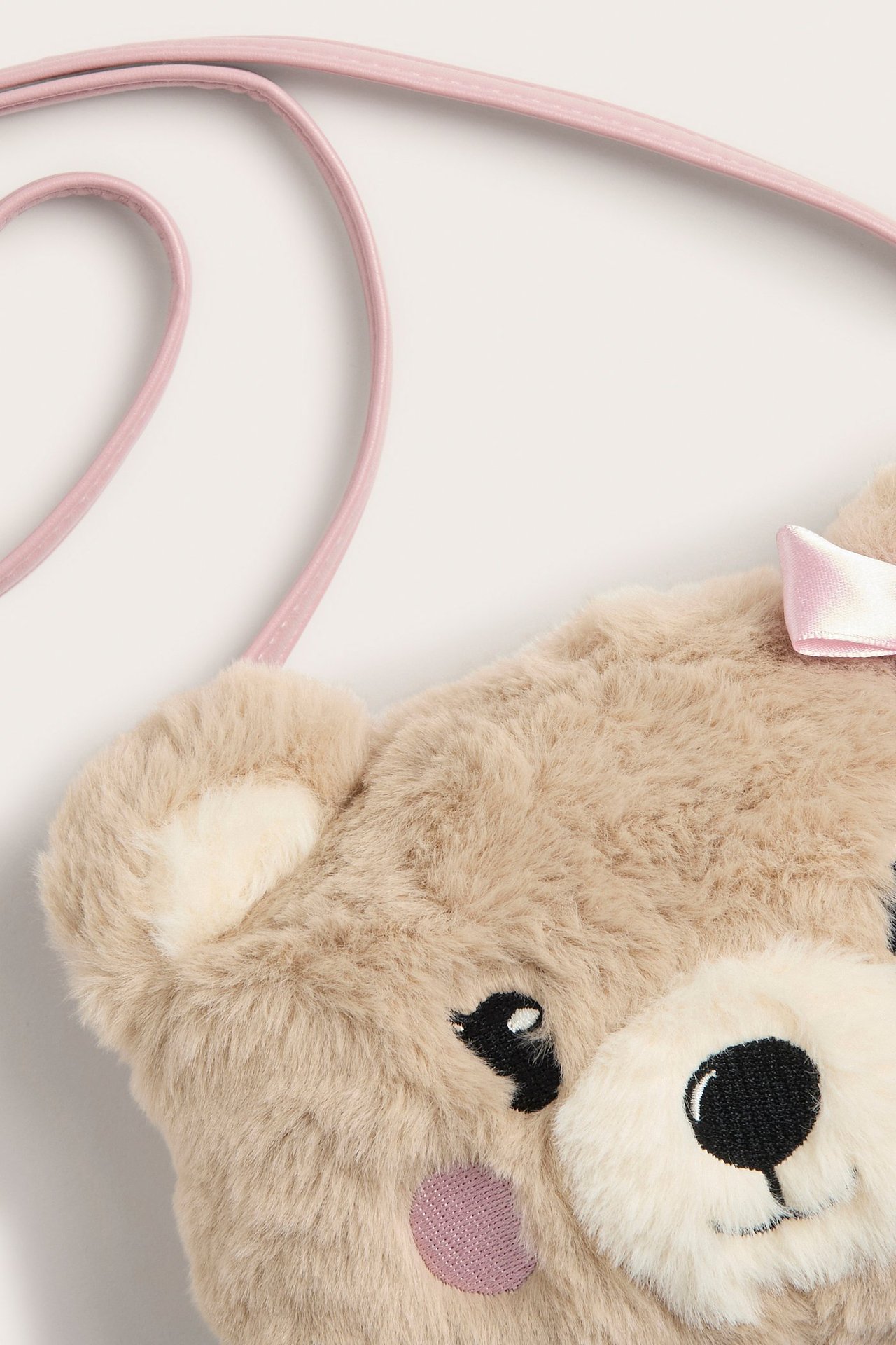Zbliżenie beżowej puszystej torebki na ramię w kształcie misia z różowym paskiem i kokardką.