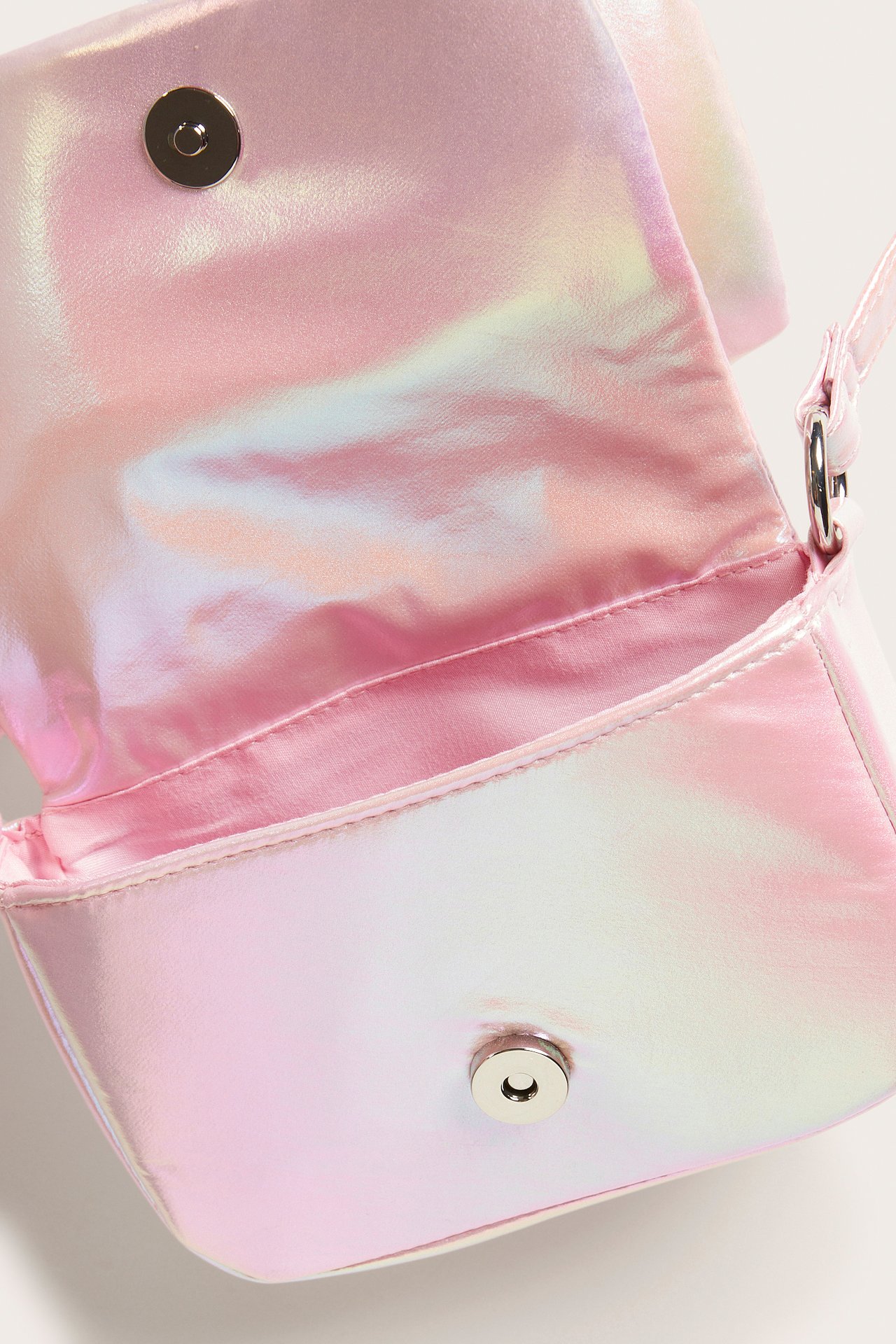 Lähikuva avoimesta irisoivasta vaaleanpunaisesta olkalaukusta, jossa on magneettikiinnitys.