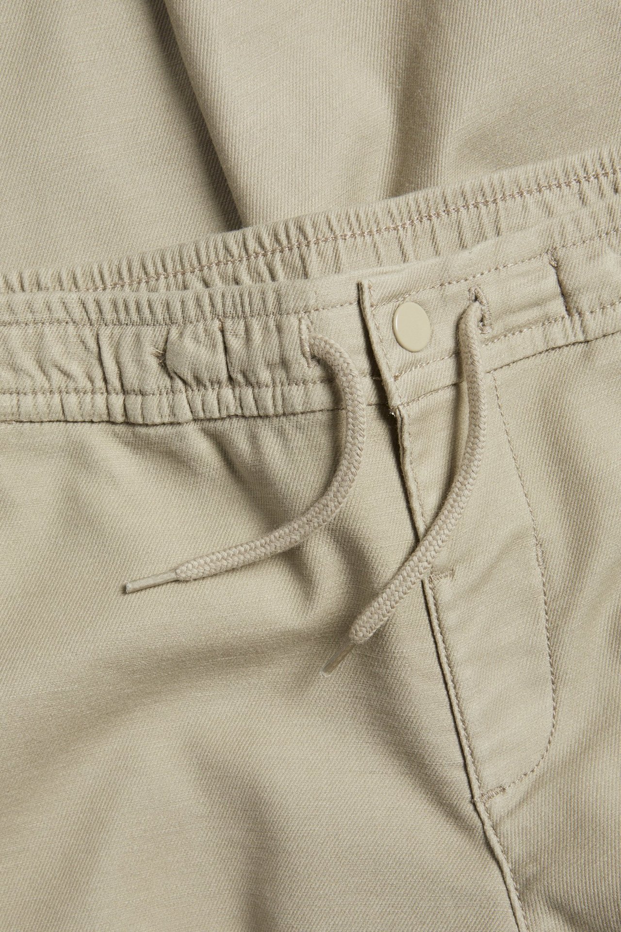 Zbliżenie na dziecięce spodnie chino w kolorze khaki z elastyczną talią, sznurkiem i zatrzaskiem.
