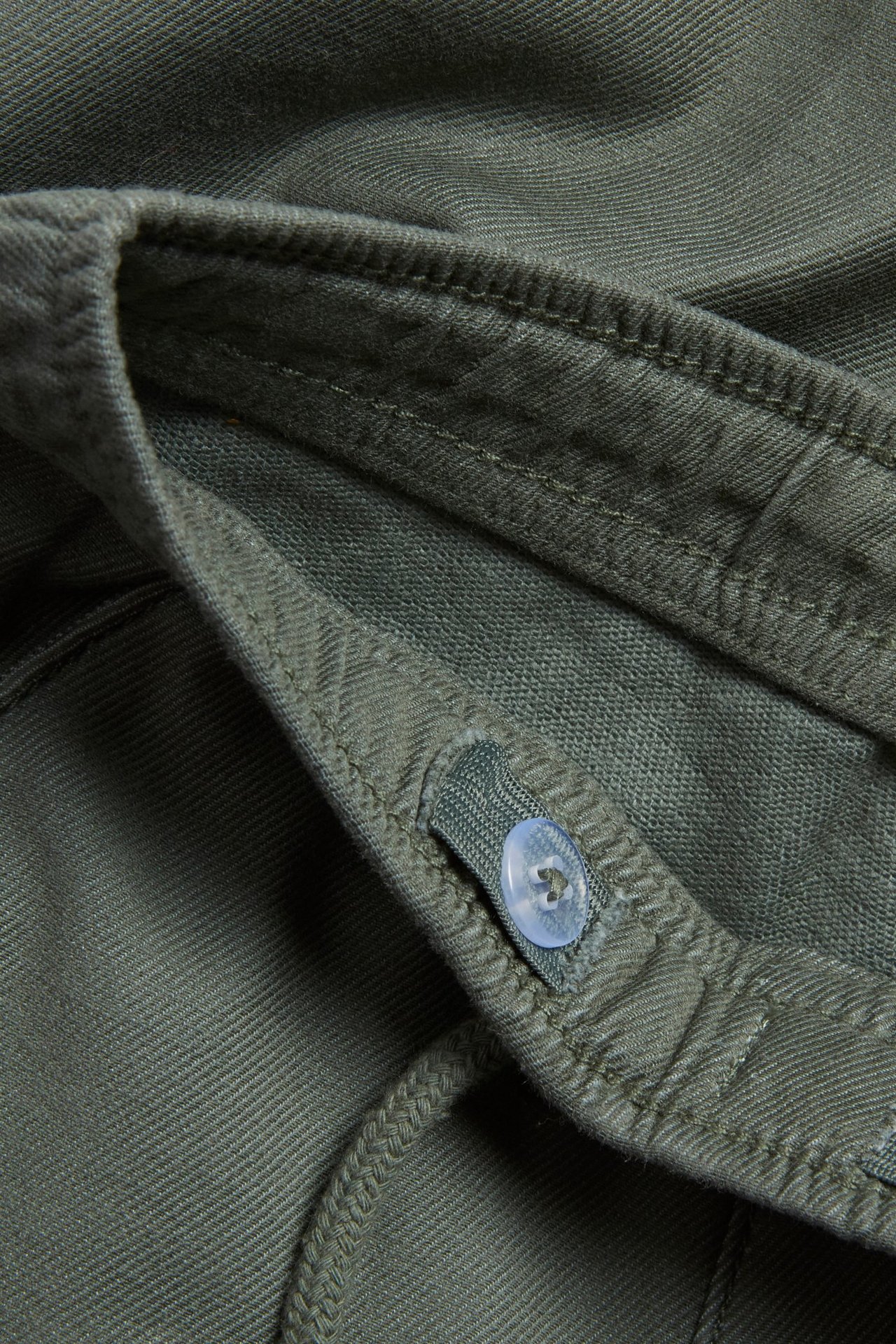 Zbliżenie na ciemnozielone chinosy dziecięce z mieszanki bawełny z jasnym guzikiem i sznurkiem.