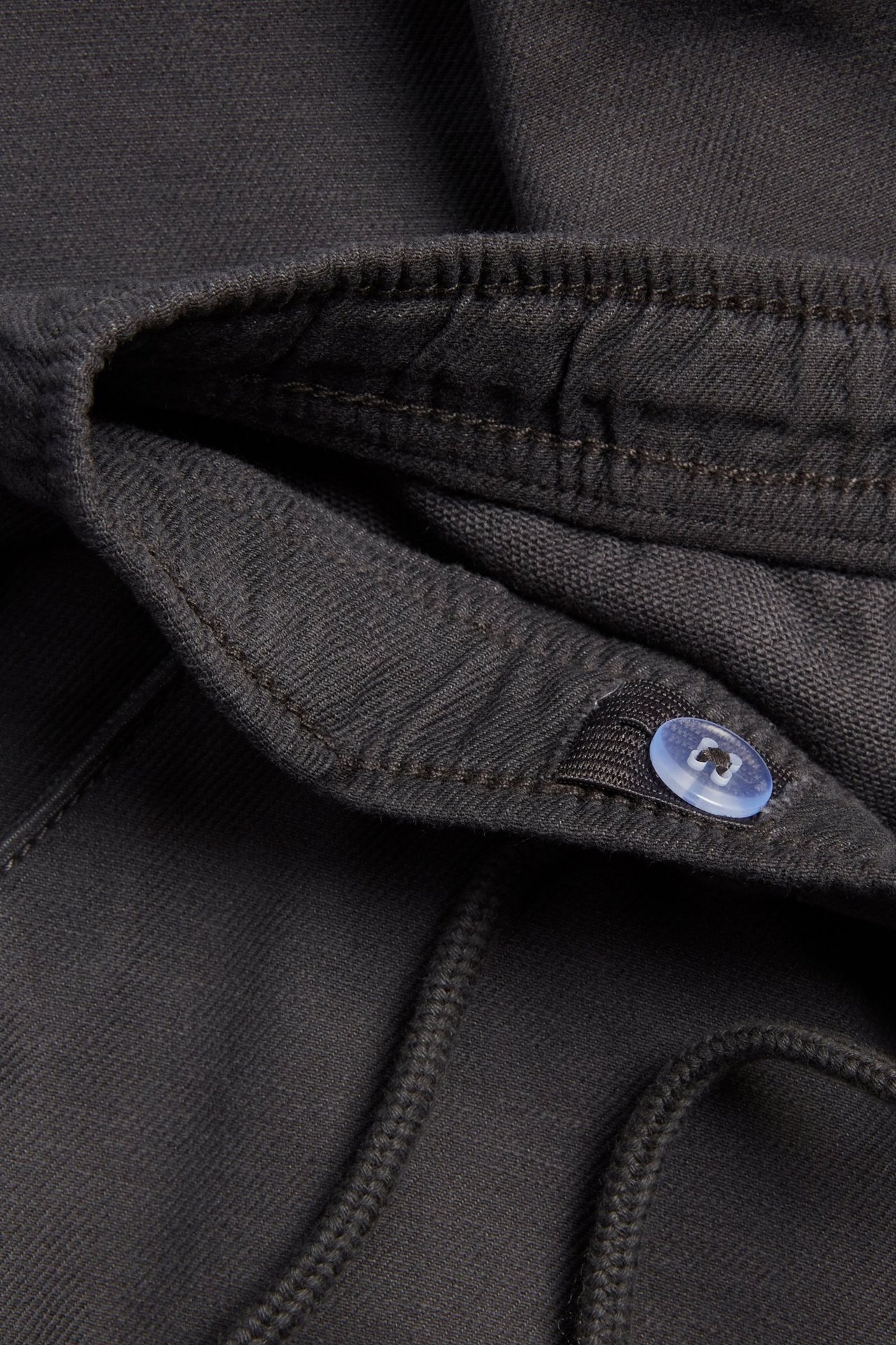 Zbliżenie na pas czarnych dziecięcych chinosów z mieszanki bawełny z gumką, sznurkiem i jasnoniebieskim zatrzaskiem.